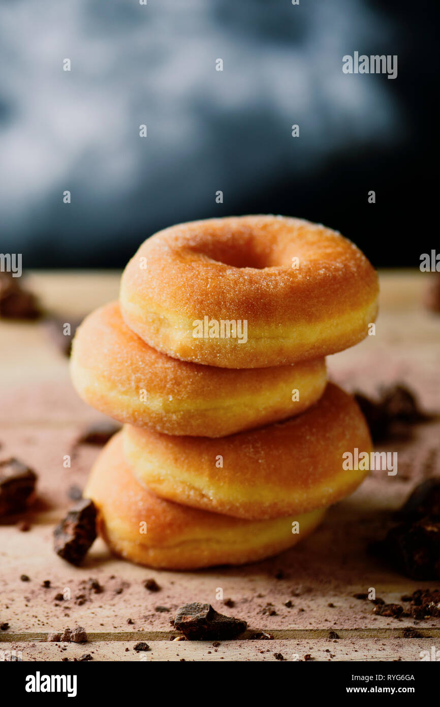a stack of sugar glazed donuts on a rustic wooden table sprinkled with small pieces of chocolate Stock Photo