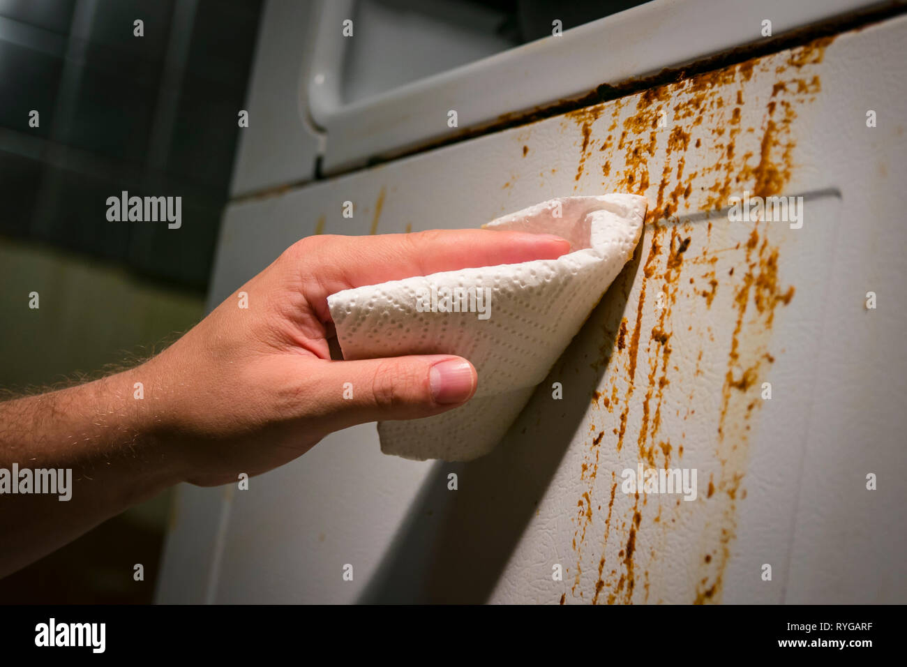 Hand cleaning baked on kitchen grime on side of oven appliance, using paper towel and cleaner. Stock Photo