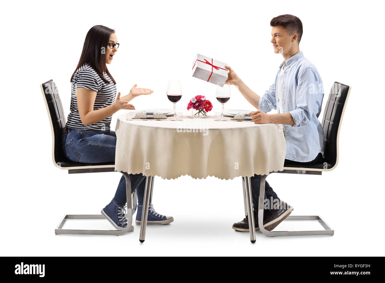 Young male giving a present to a young female at a restaurant table isolated on white background Stock Photo