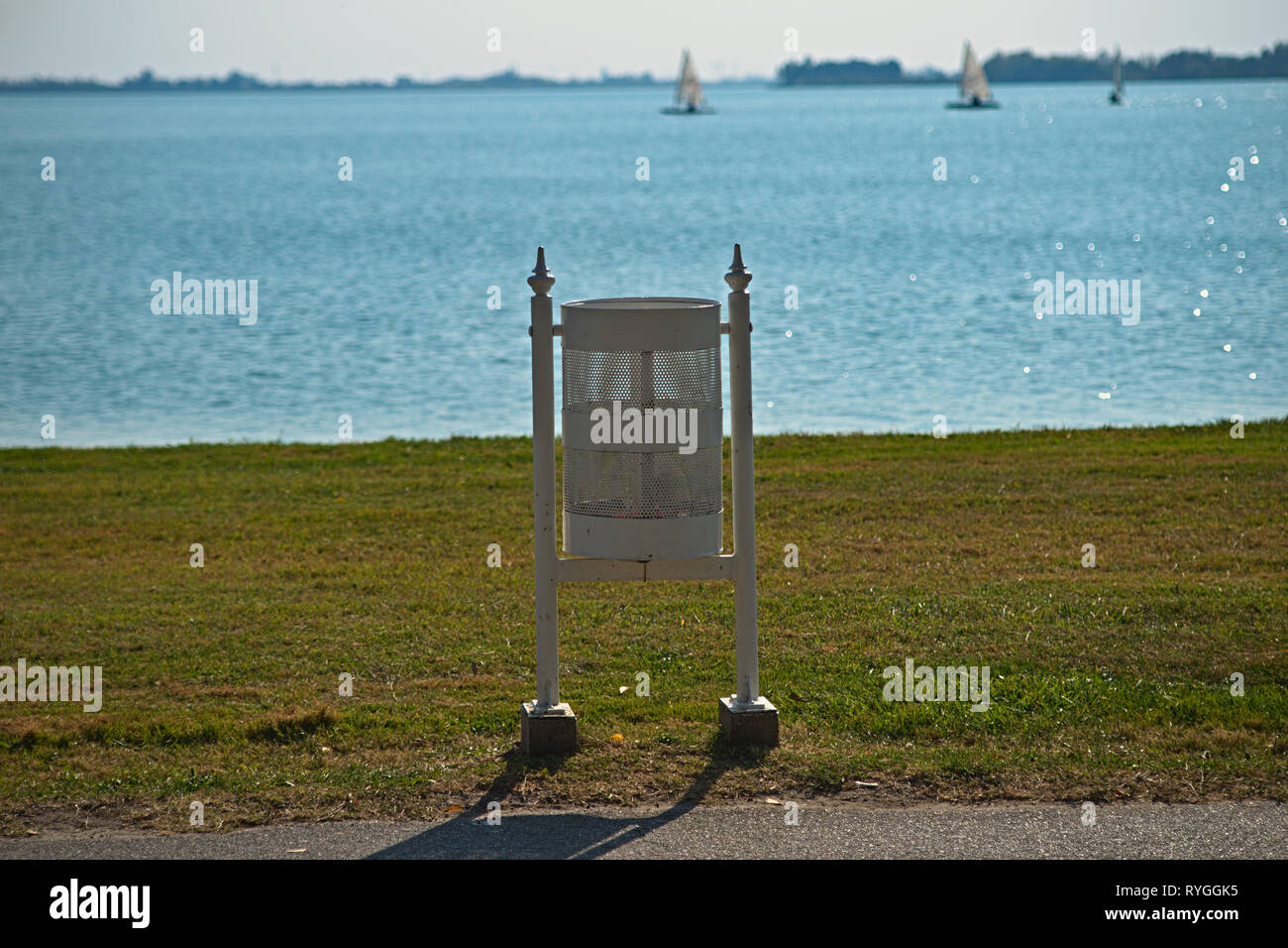 White trash can on boardwalk looking at grass field and lake Stock Photo