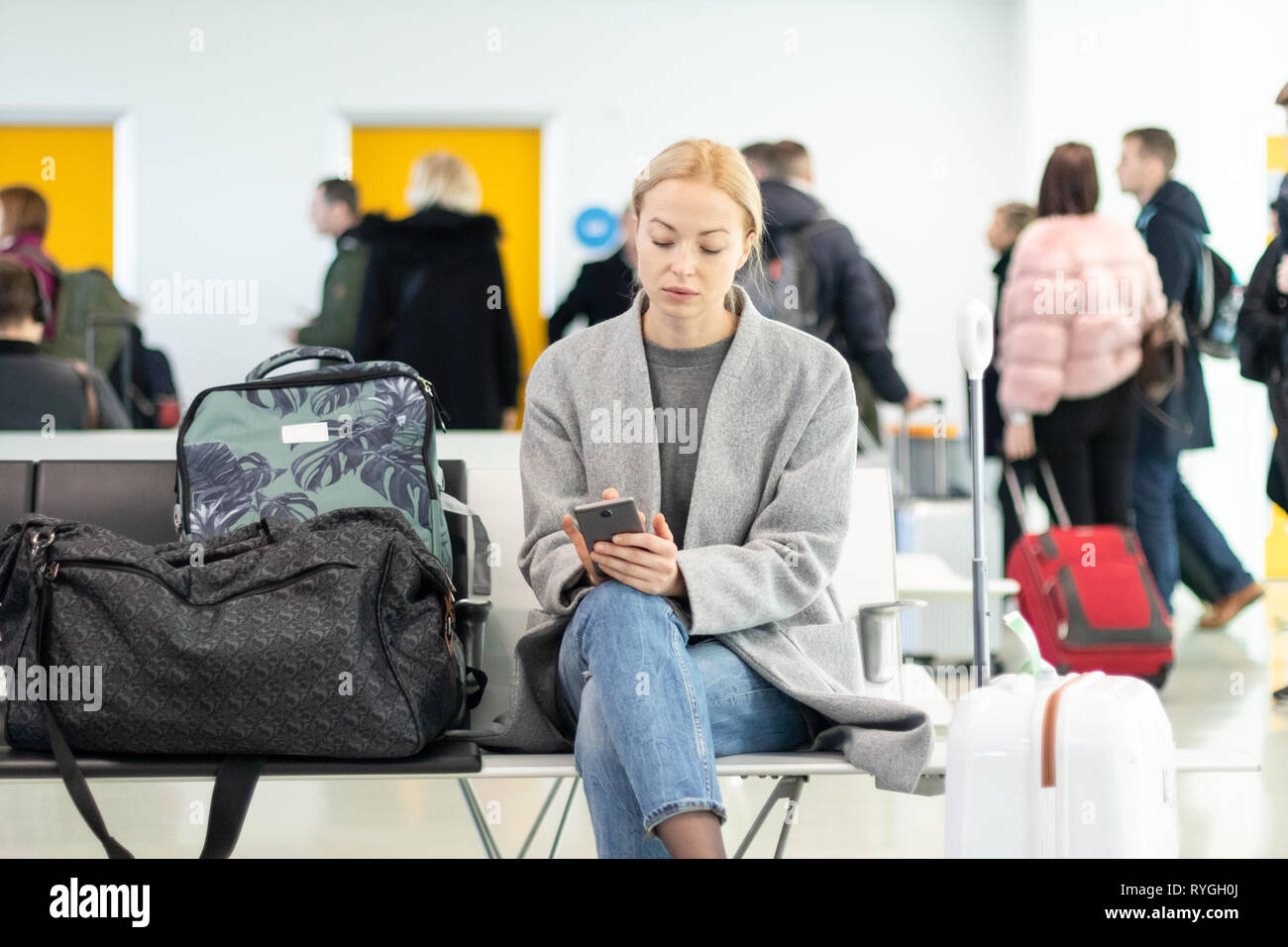 Female traveler using her cell phone while waiting to board a plane at departure gates at airport terminal. Stock Photo