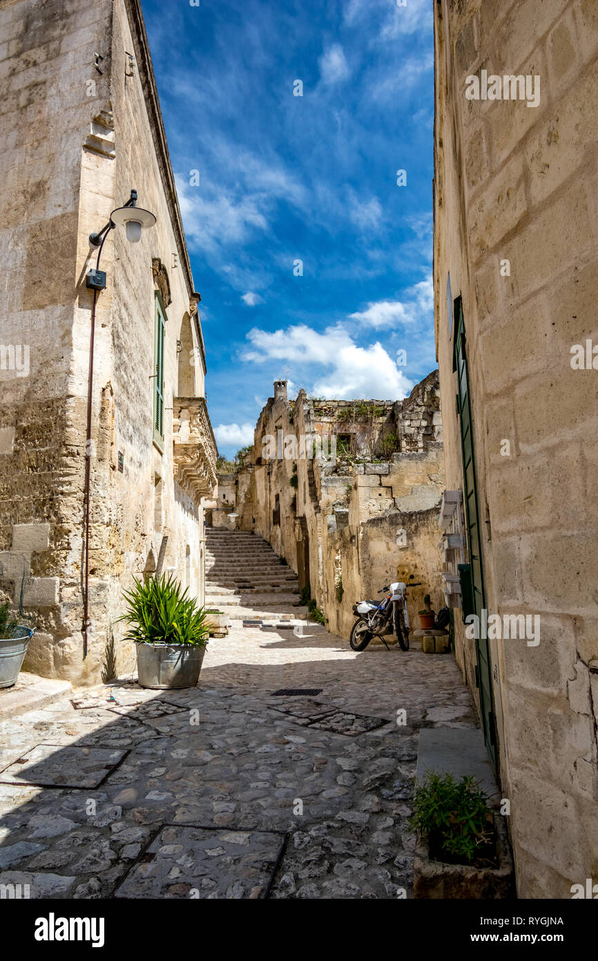 Summer day scenery street view of the amazing ancient town of the Sassi with motorbike and white puffy clouds moving on the Italian blue sky. Matera, Basilicata, Italy Stock Photo