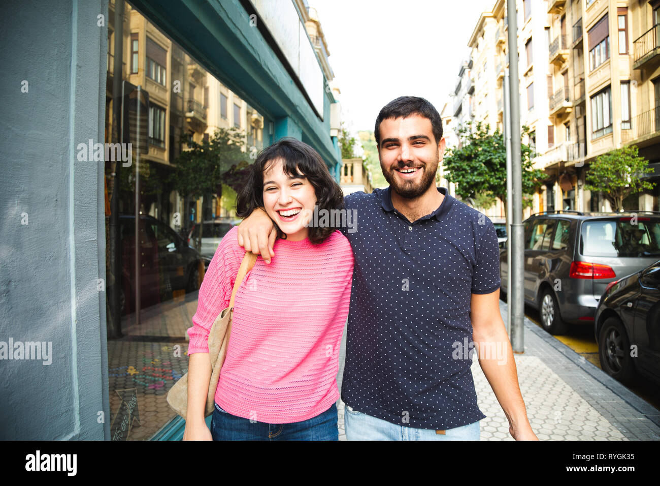 Happy and attractive young couple laughing while walking on the city street Stock Photo