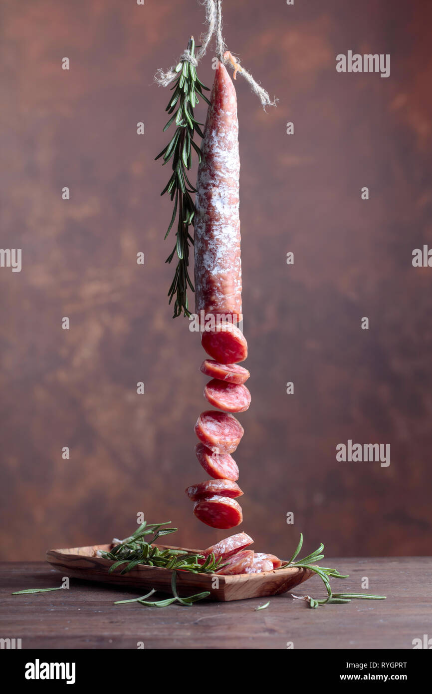 Dry-cured sausage with rosemary on a old wooden table. Stock Photo