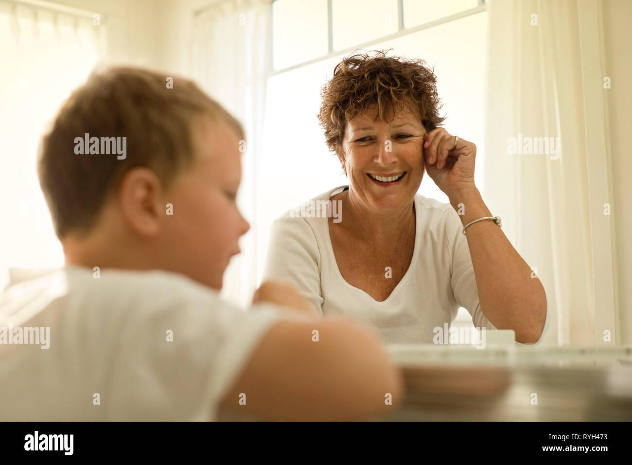 Smiling mature woman sitting at a table with her young grandson. Stock Photo