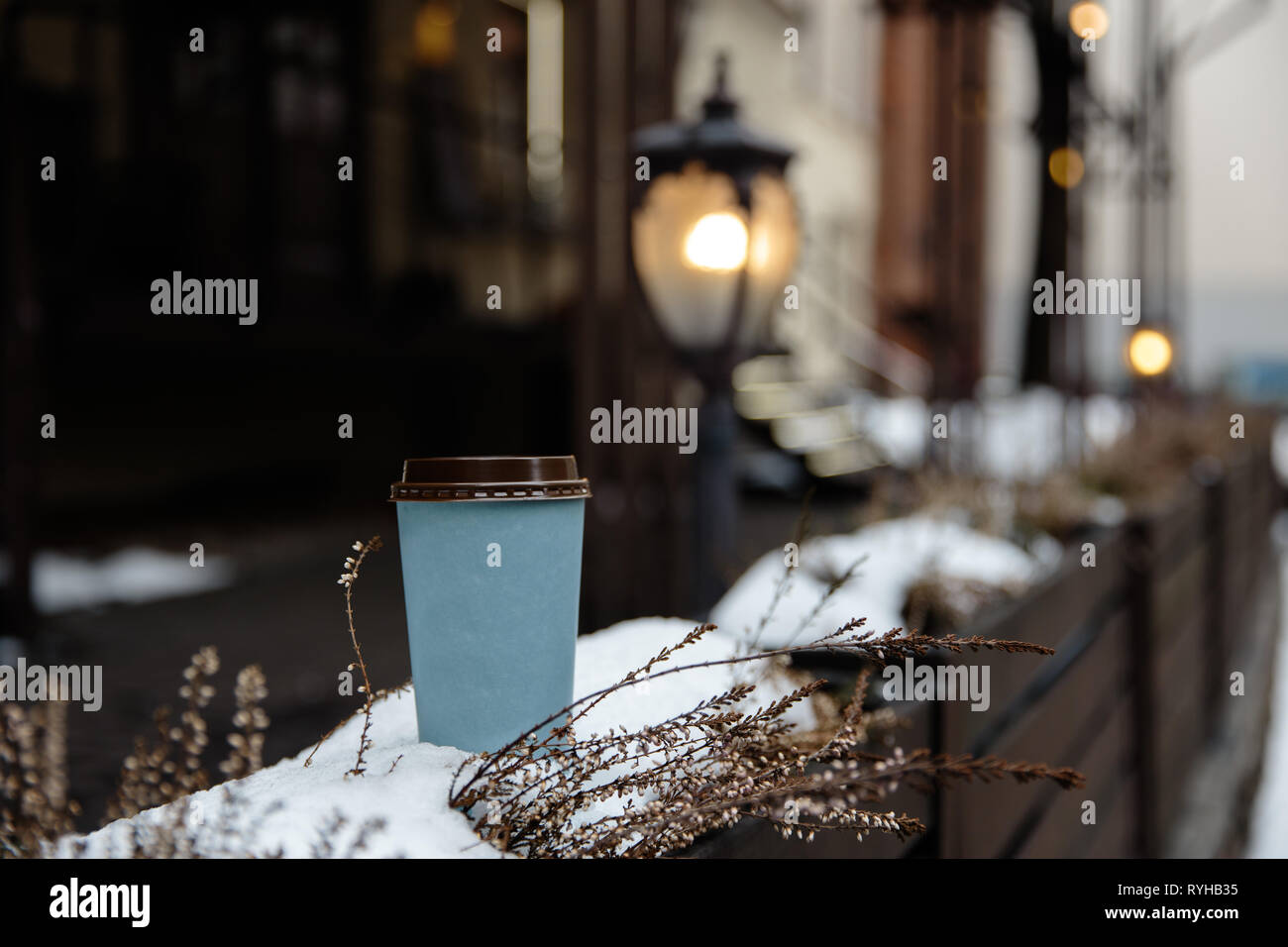 Mockup ad: a blank paper cup standing on a fence in an old town
