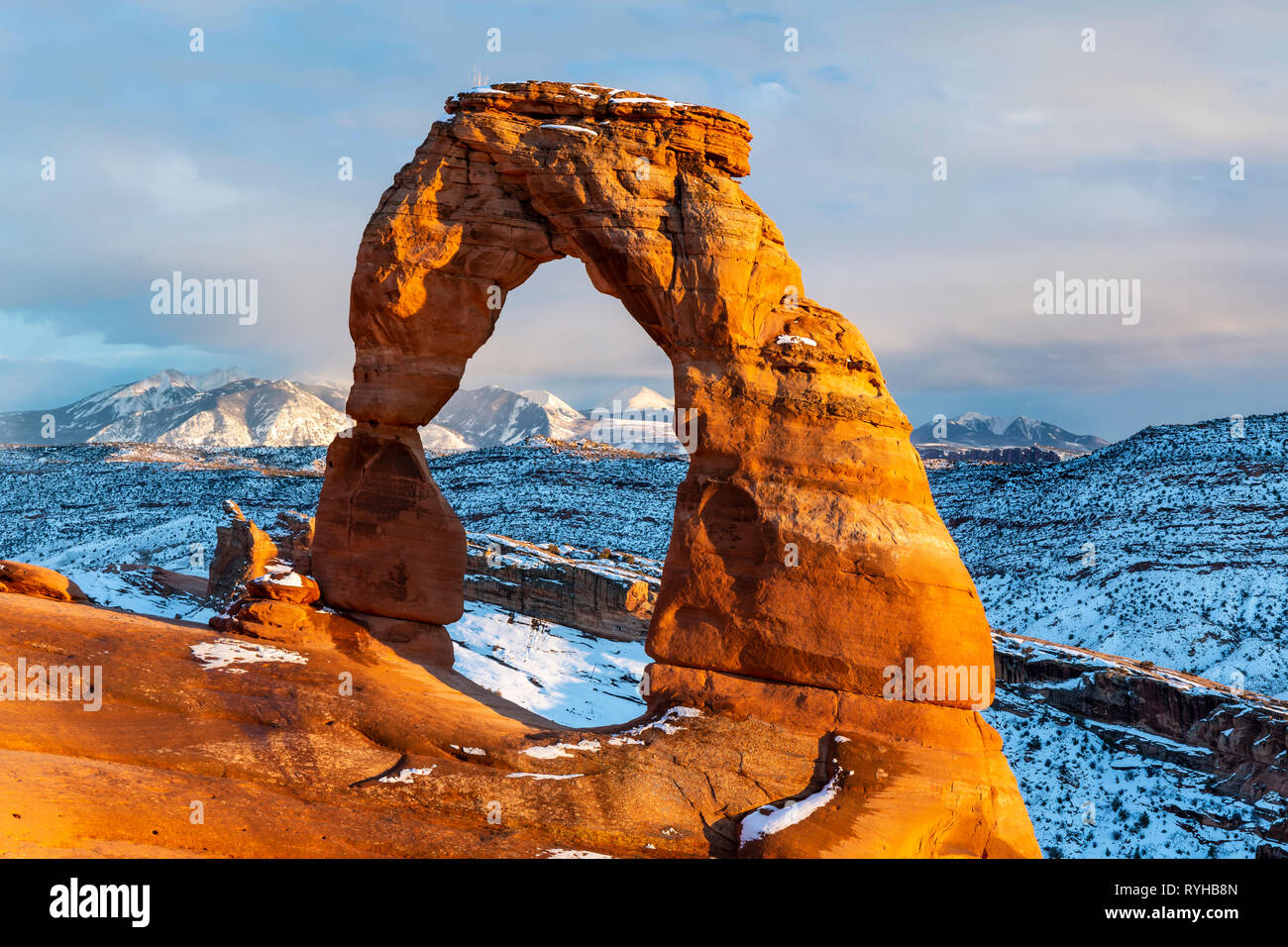 iconic Delicate Arch lit with bright golden hour light with the La Sal Mountains behind after a Febraury 2019 snowstorm in Arches National Park, Moab, Stock Photo