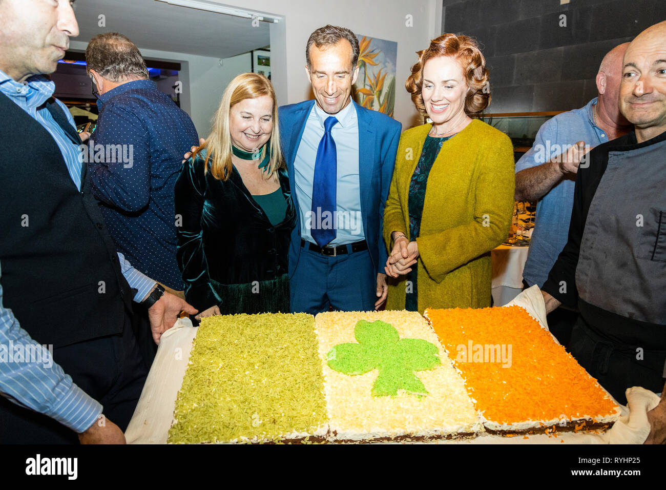 Costa Adeje Golf Club, Adeje, Tenerife, Spain. 13th March 2019. A giant tricolor cake with a green shamrock is presented at a St. Patricks Day Gala dinner in the Golf Costa Adeje club house, hosted by the Honorary Irish Consul, Álvaro de la Bárcena Argany, with his wife Mairead Ryan, (right), and Tessa Willis García Talavera, (left), vice consul of the Consulate of Ireland in Tenerife. © Phil Crean Credit: Phil Crean A/Alamy Live News Stock Photo