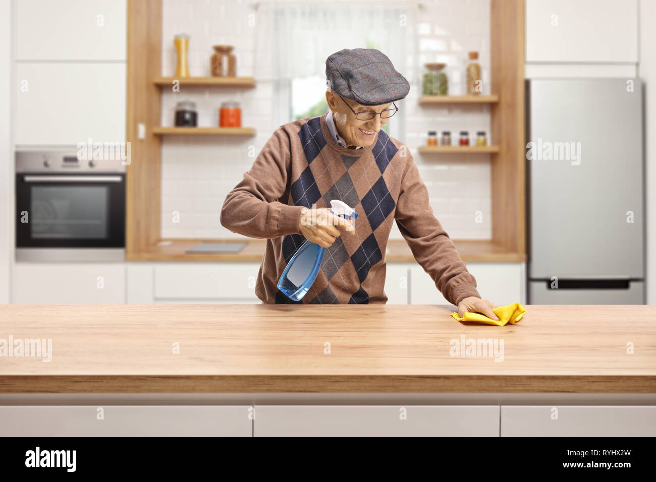 Elderly man cleaning a wooden counter in a kitchen Stock Photo