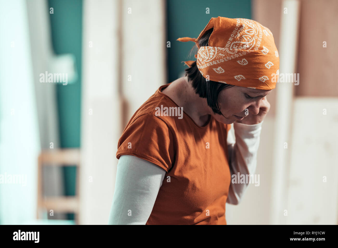 Female carpenter with head kerchief during serious mobile phone conversation with client in carpentry woodwork workshop Stock Photo