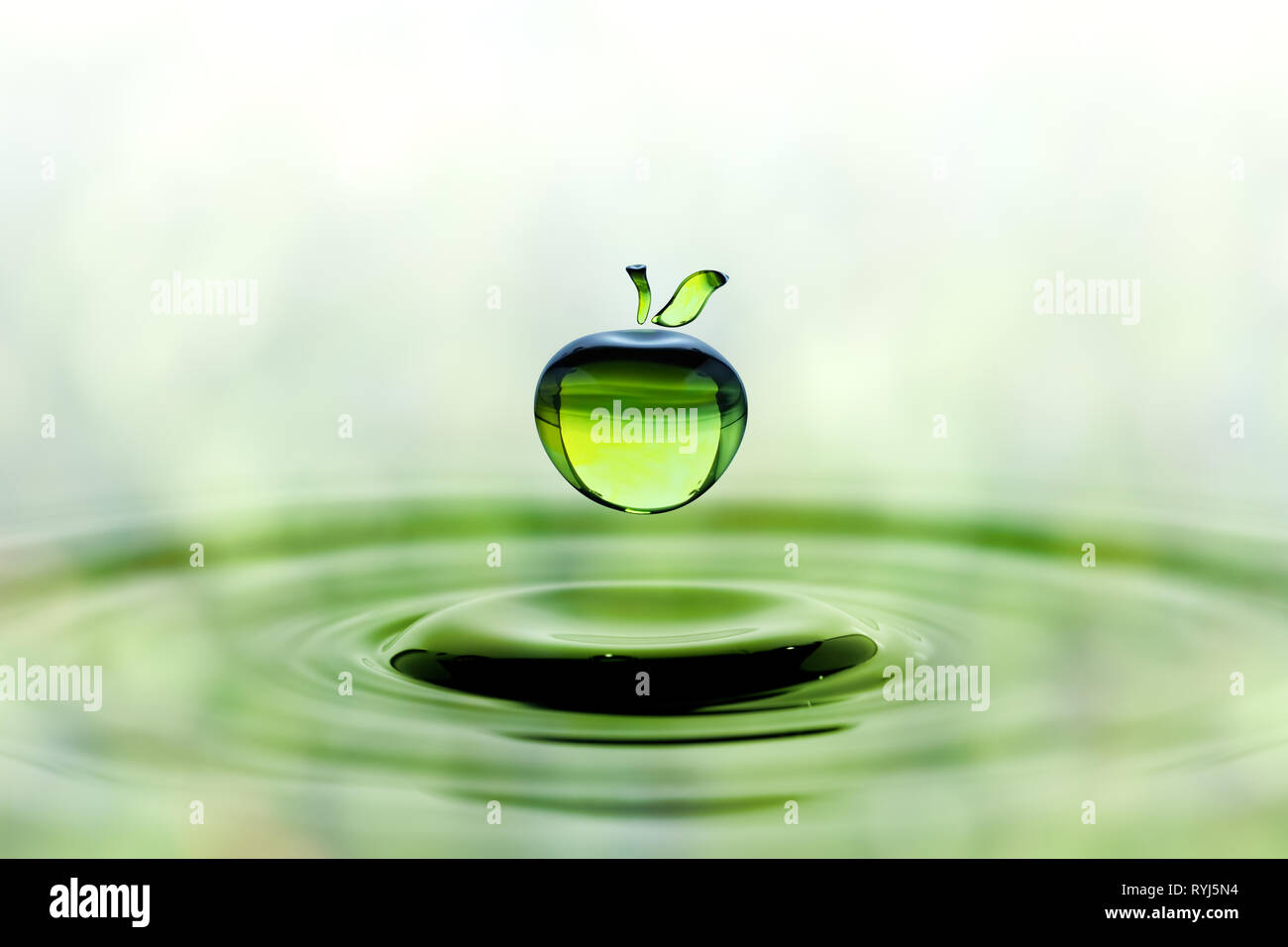 Rain drop in shape of green apple falling on blue water surface. Green blurred pattern in background. Stock Photo
