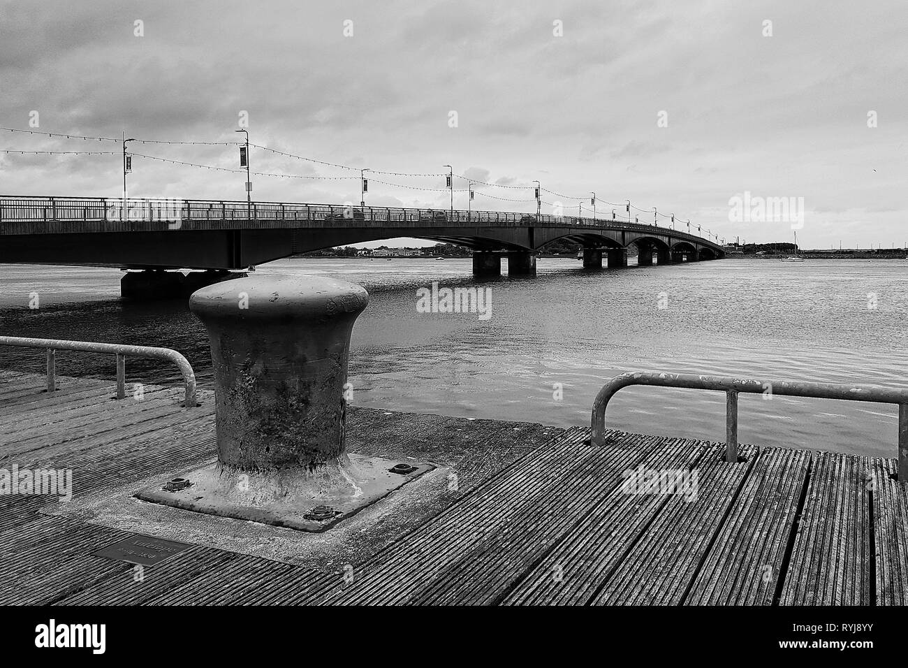 Black and white photo of the bollard on wooden deck with bridge in the background - Wexford Ireland Stock Photo