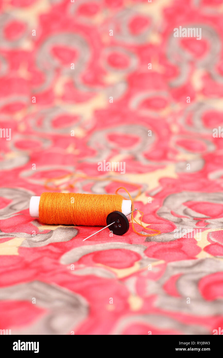 Picture of orange sewing thread, needle and button. Isolated on the colorful background. Stock Photo