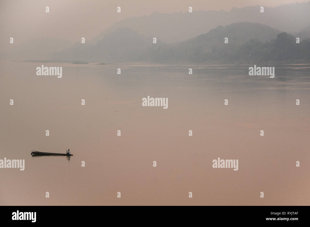 Lost in Haze - Fisherman on his boat on the Mekong during Burning Season in Laos, hazy, pastel colored air. Stock Photo