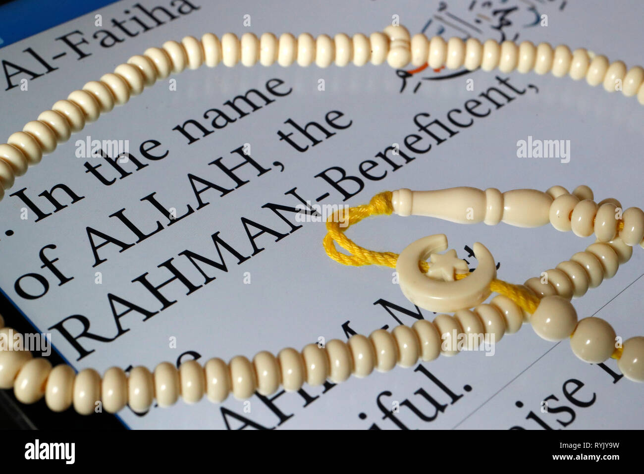 Digital Quran on a smartphone and muslim prayer beads.  English translation. In the name of Allah.  Close-up. Stock Photo