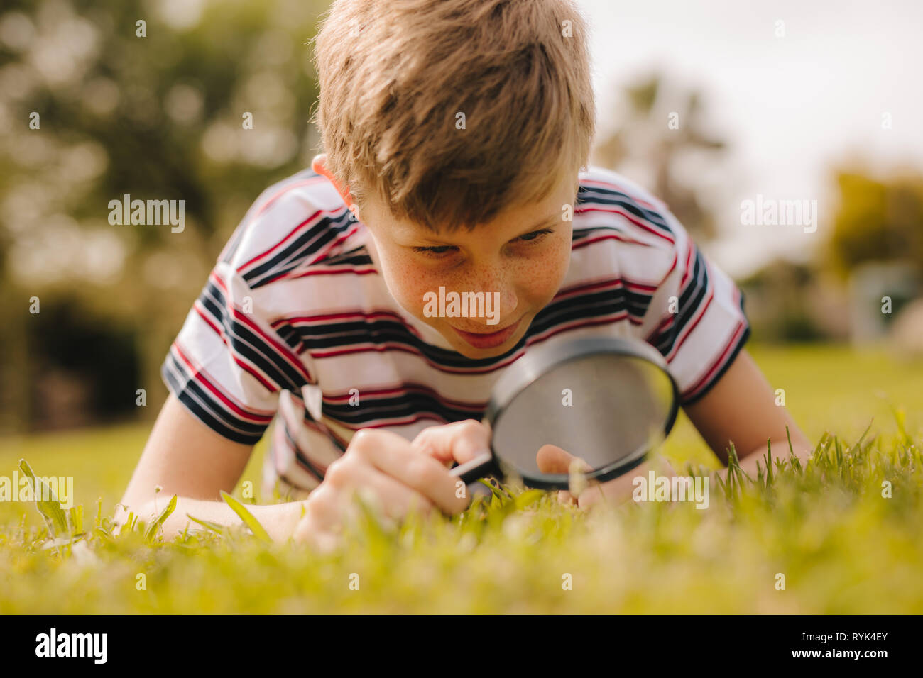 Young caucasian boy exploring garden with his magnifying glass. Cute boy looking through magnifying glass at the grass. Stock Photo