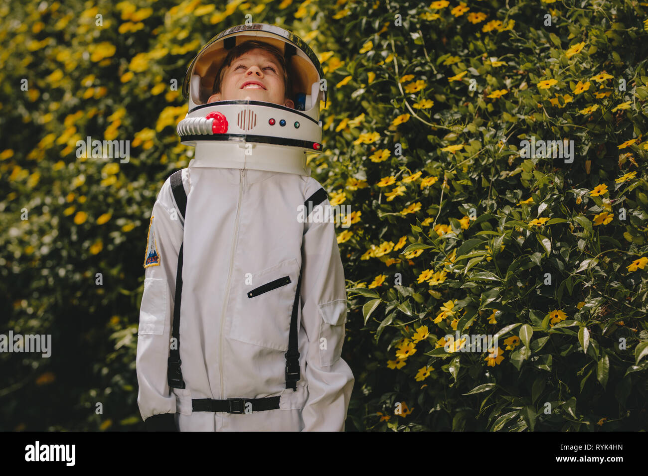 Boy wearing space suit and helmet standing outdoors and looking up. Cute boy in astronaut dress playing outdoors. Stock Photo