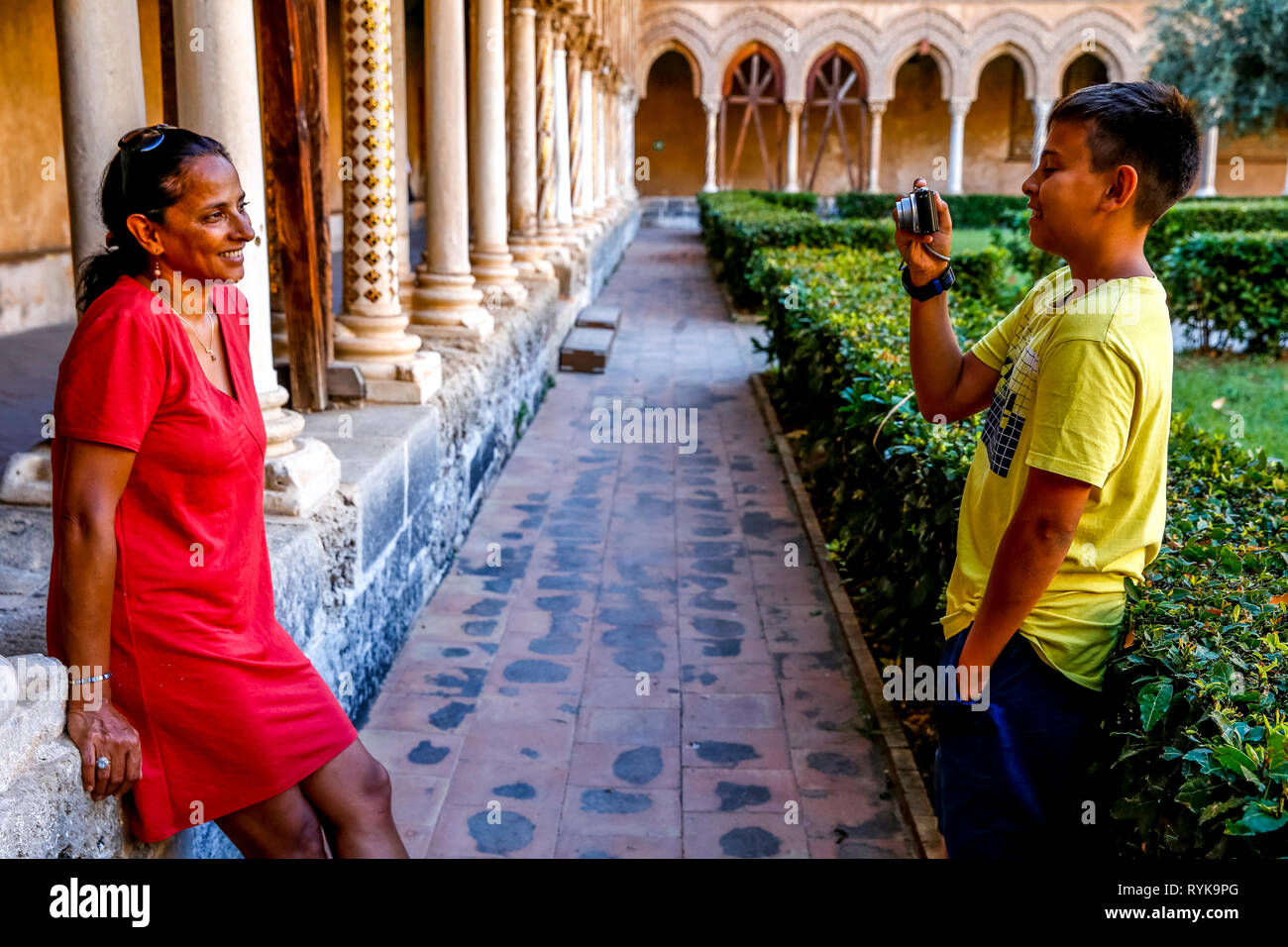 12-year-old boy taking a photograph of his mother in the cloister of Monreale cathedral, Sicily (Italy). Stock Photo