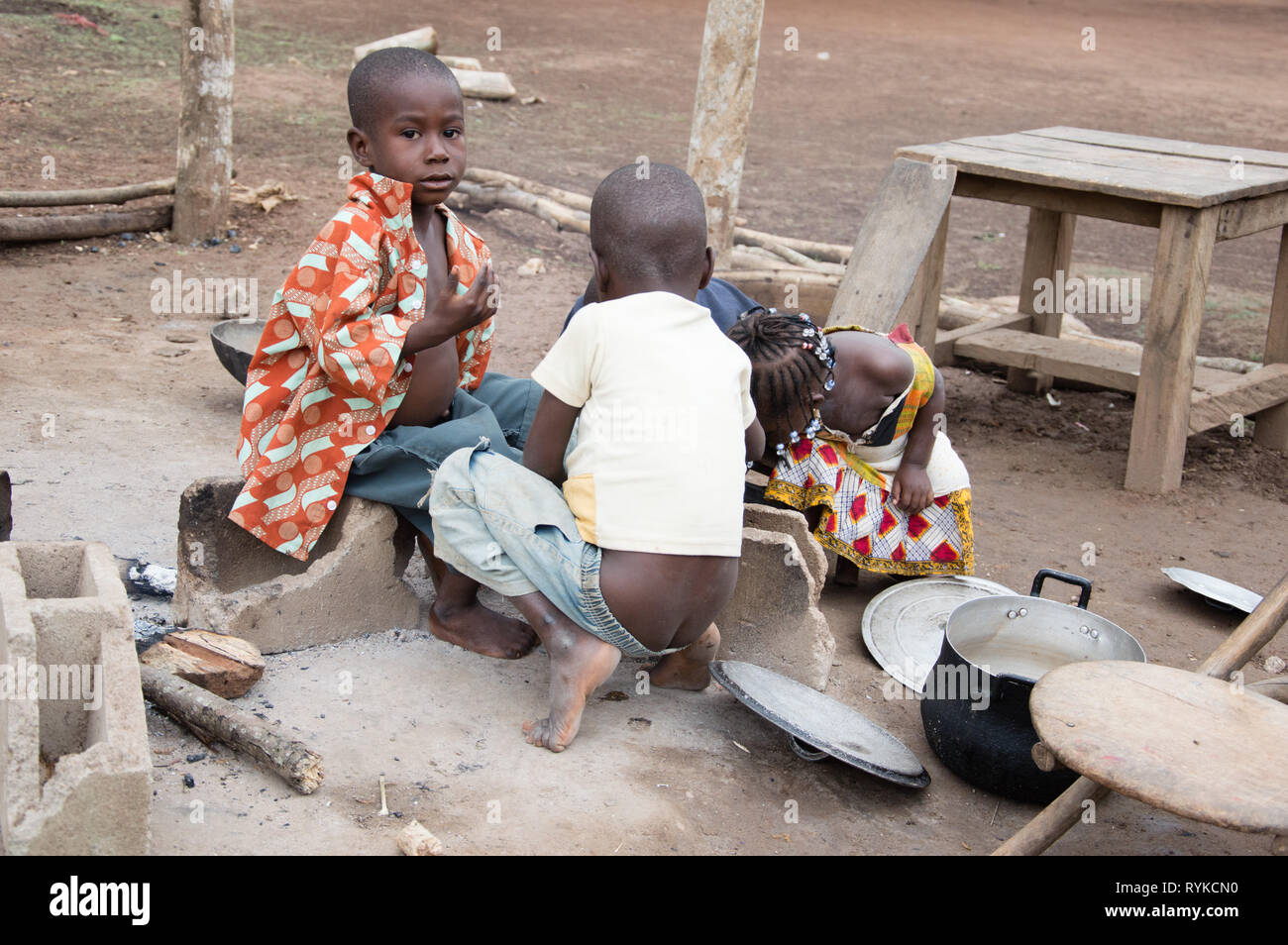 Anekro, Ivory Coast - 27 August 2015: the children eat in the morning group in yard near a fire. Four children sitting around a meal shared together Stock Photo