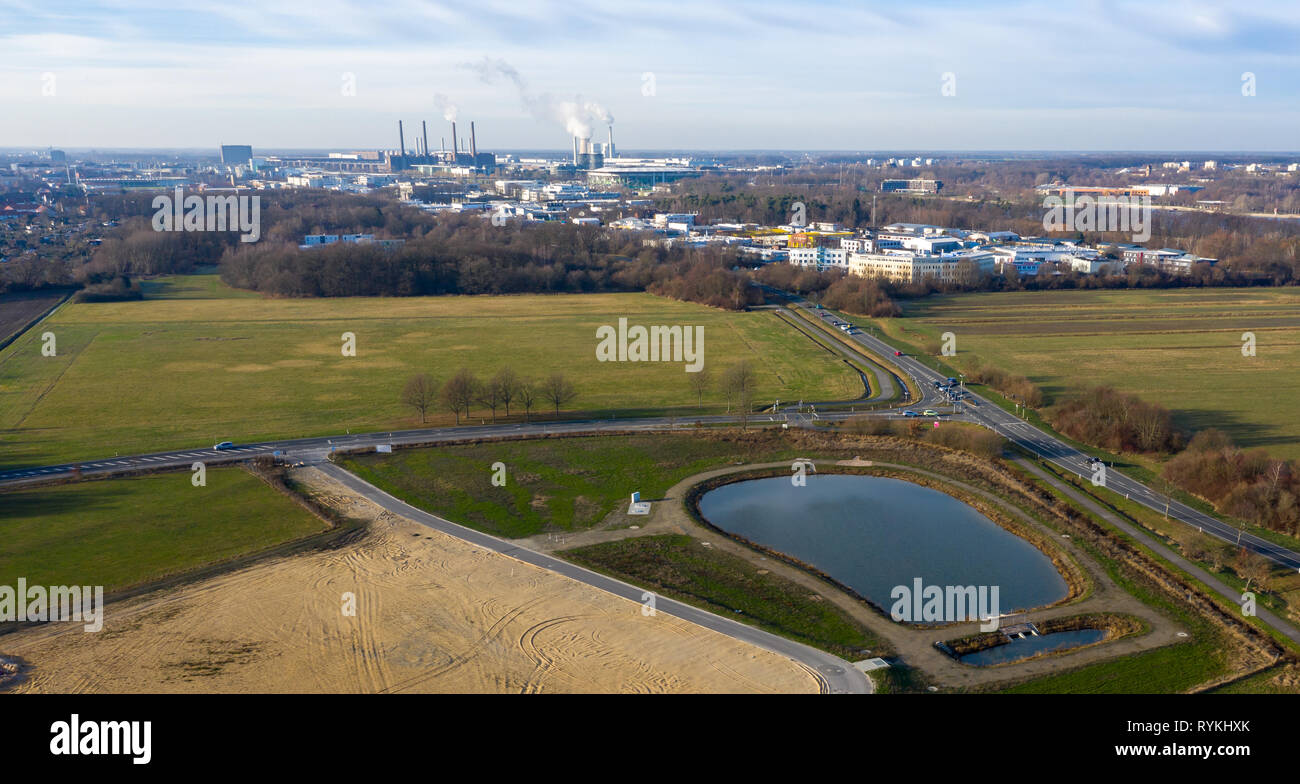Aerial view of a rainwater retention basin with roads and a large meadow area and an industrial city in the background. Stock Photo