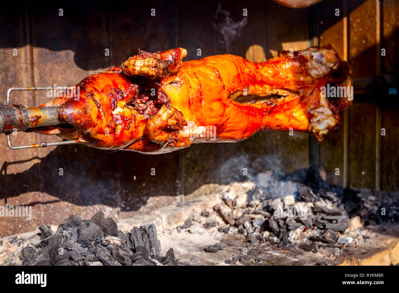 Pig is being grilled slowly on spit in traditional way, cooked with charcoal, fatty roasted meat Stock Photo