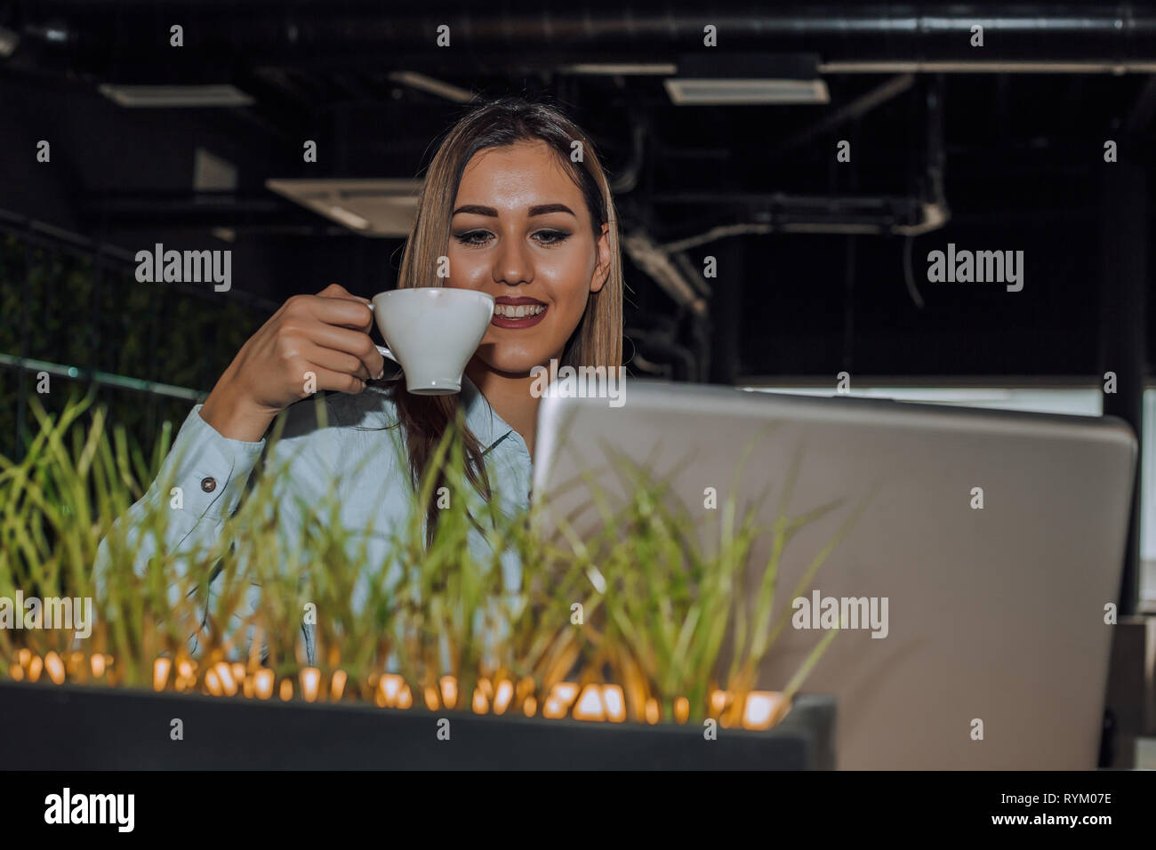 Beautiful young woman working on laptop and drinking coffee in modern ...