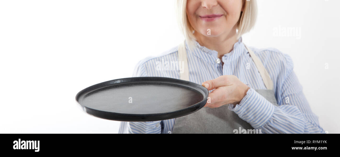 Kitchen woman waitress gives empty black plate for your advertising products isolated on white background. Mock up for use Stock Photo