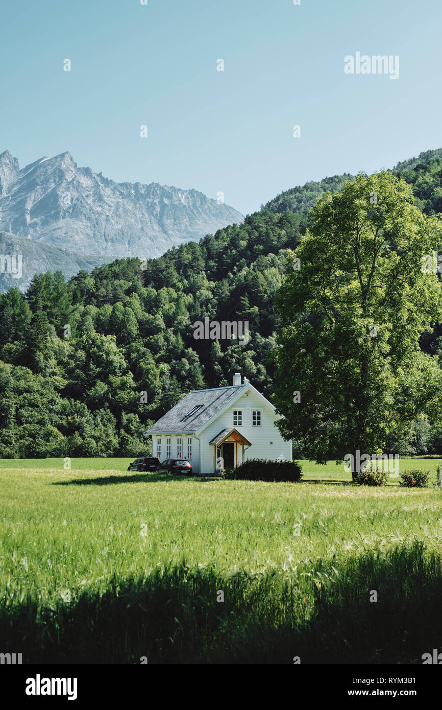 A lone white wooden paneled house in the green summer landscape of Norway - Norway house architecture Stock Photo