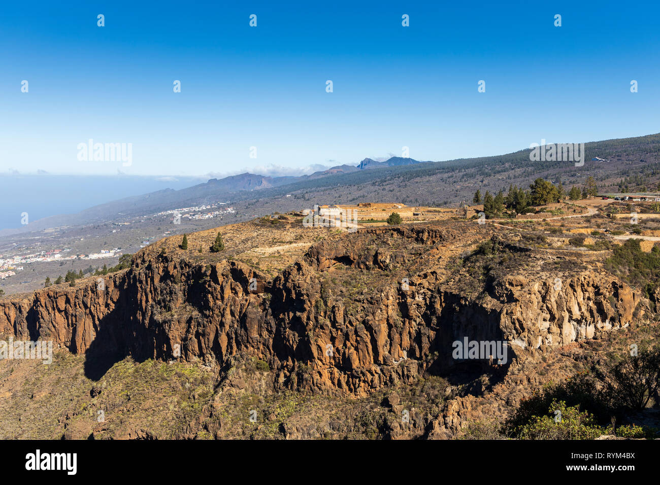View into the Barranco de Guaria and a remote finca farmhouse above the cliffside, and the cliffs of Los Gigantes on the far horizon, from Las Fuentes Stock Photo