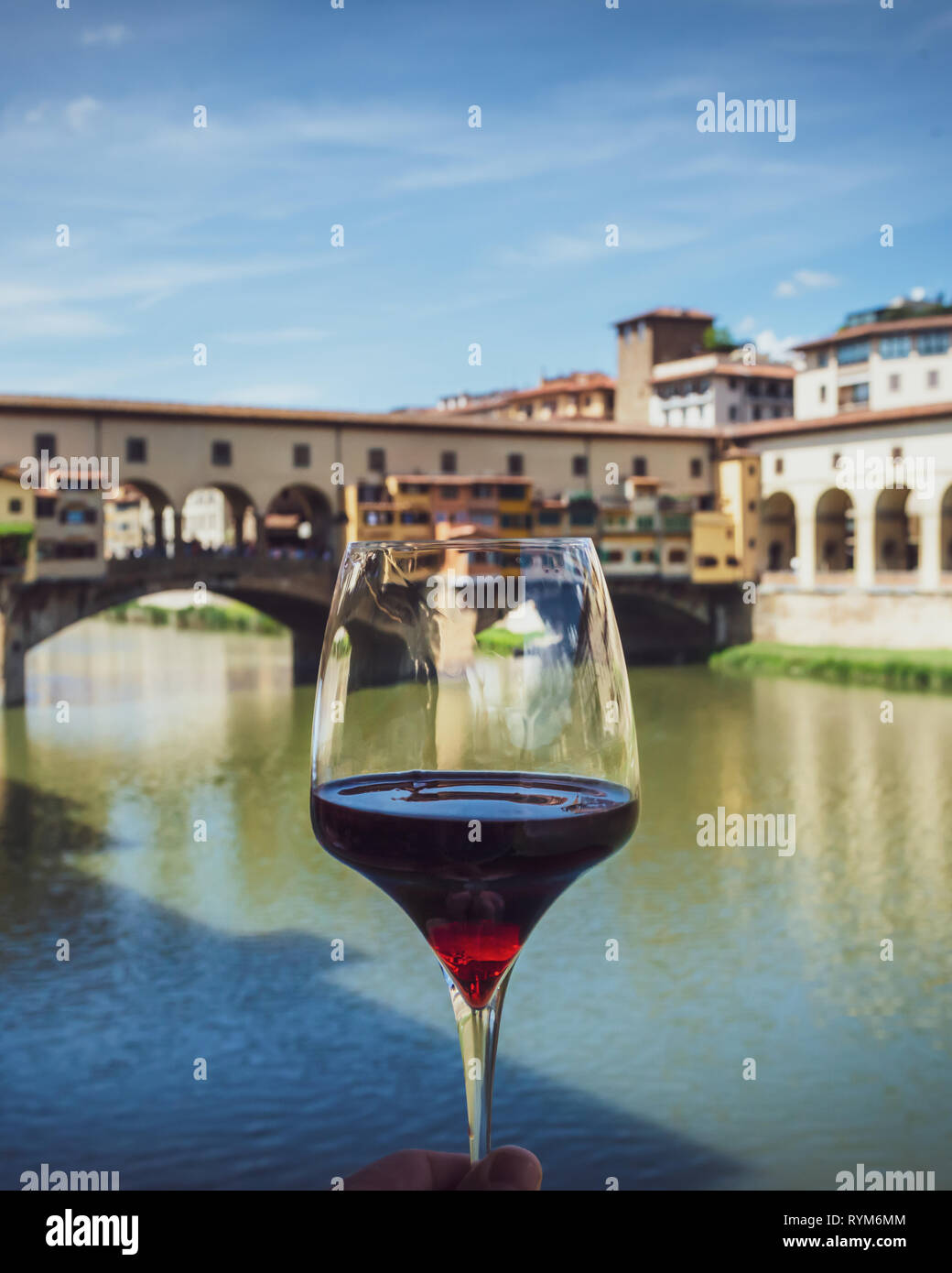 Glass of red wine on background of city and famous bridge in Florence, Italy. View from restaurant terrace on antique buildings in warm summer day. Stock Photo