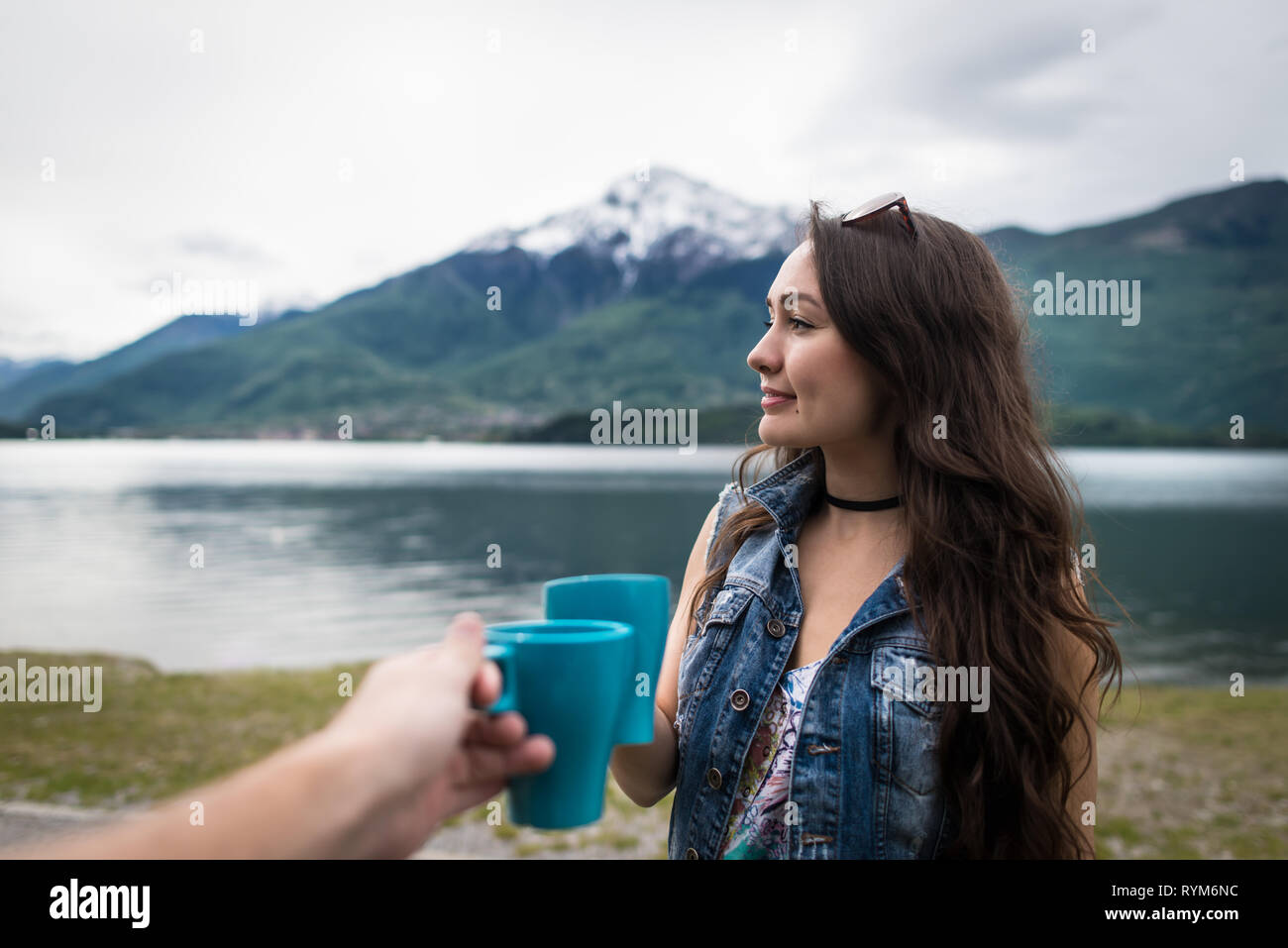 Young woman standing with cup of coffee in morning on background of mountains and lake in Como, Italy. Smiling girl celebrate holidays with boyfriend. Stock Photo