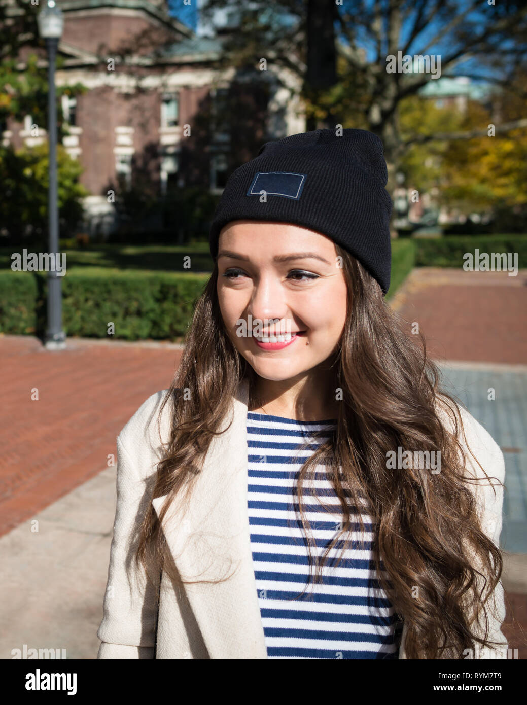 Beautiful young woman stands near buildings of Columbia University in New York, USA. Stylish Kazakh female student smiling on background of campus. Stock Photo