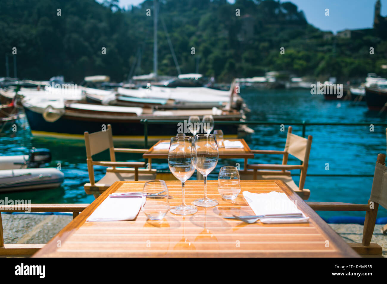 Restaurant with a view in Portofino, Italy. Table serving for dinner with wine glasses on background of marina, small boats and sea in warm summer day Stock Photo