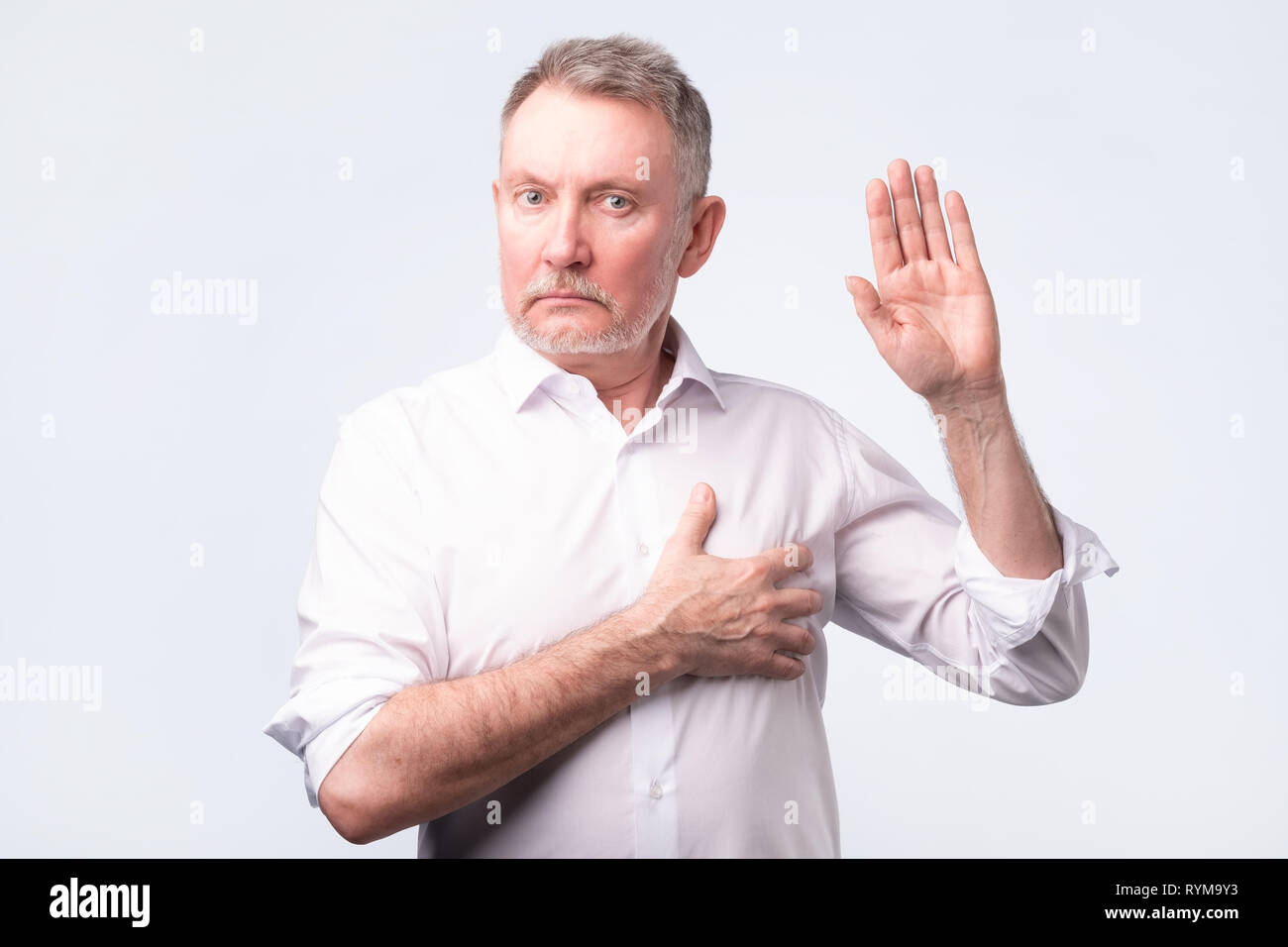 Handsome senior man in white shirt making an oath. Give a promise. Stock Photo