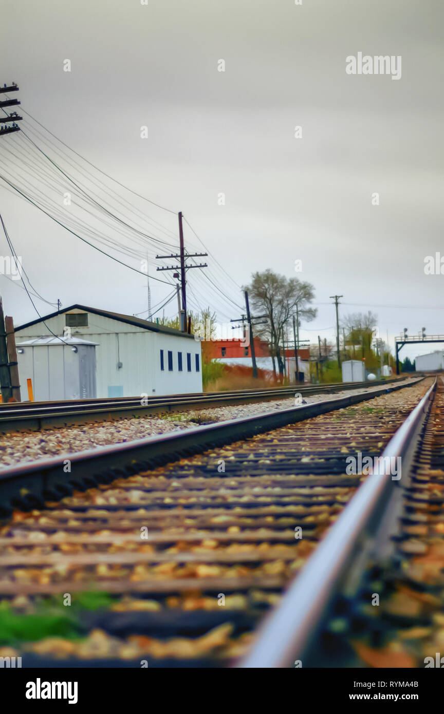 A low angle shallow depth of field shot of railway tracks disappearing into the distance. A white shed along with a signal gantry is also visible. Stock Photo