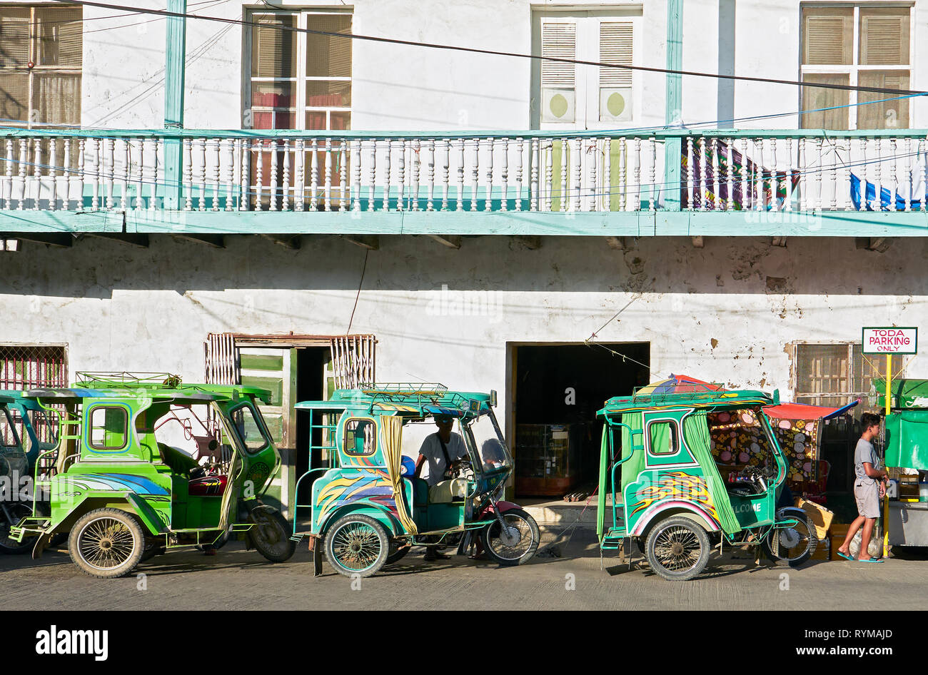 Romblon, Romblon Province, Philippines: Three green tricycles in the town center waiting for passengers, old buildings in background Stock Photo