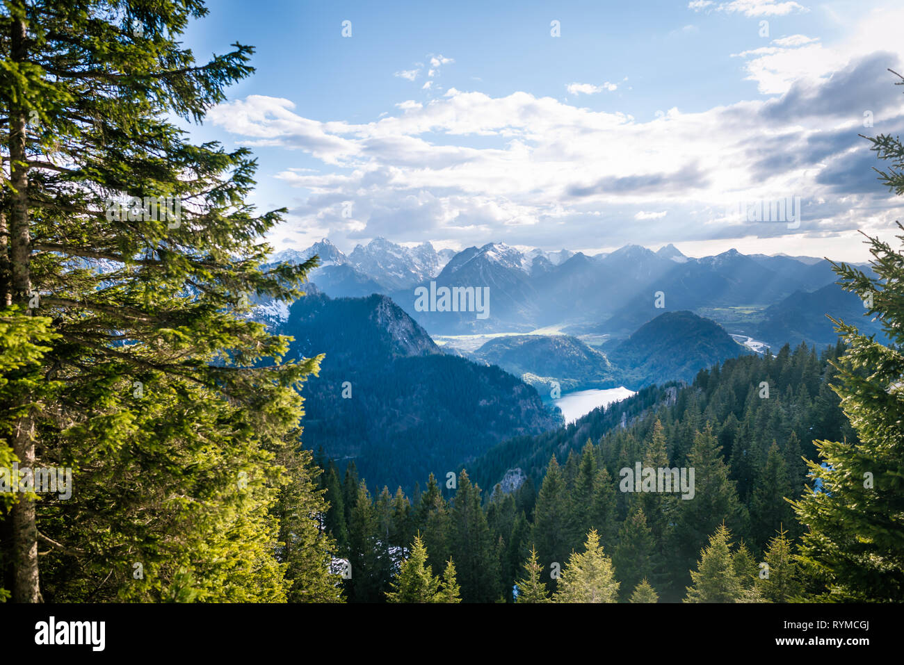 Scenic landscape overlooking the mountains with snowy tops. Sunlight rays falling through the clouds on beautiful valley with lakes and forest. Stock Photo