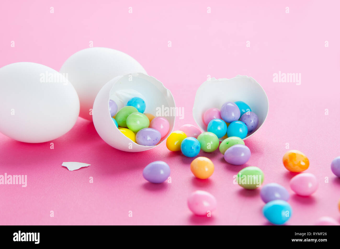 colourful easter eggs spilling out of a white egg shell on a pink background Stock Photo