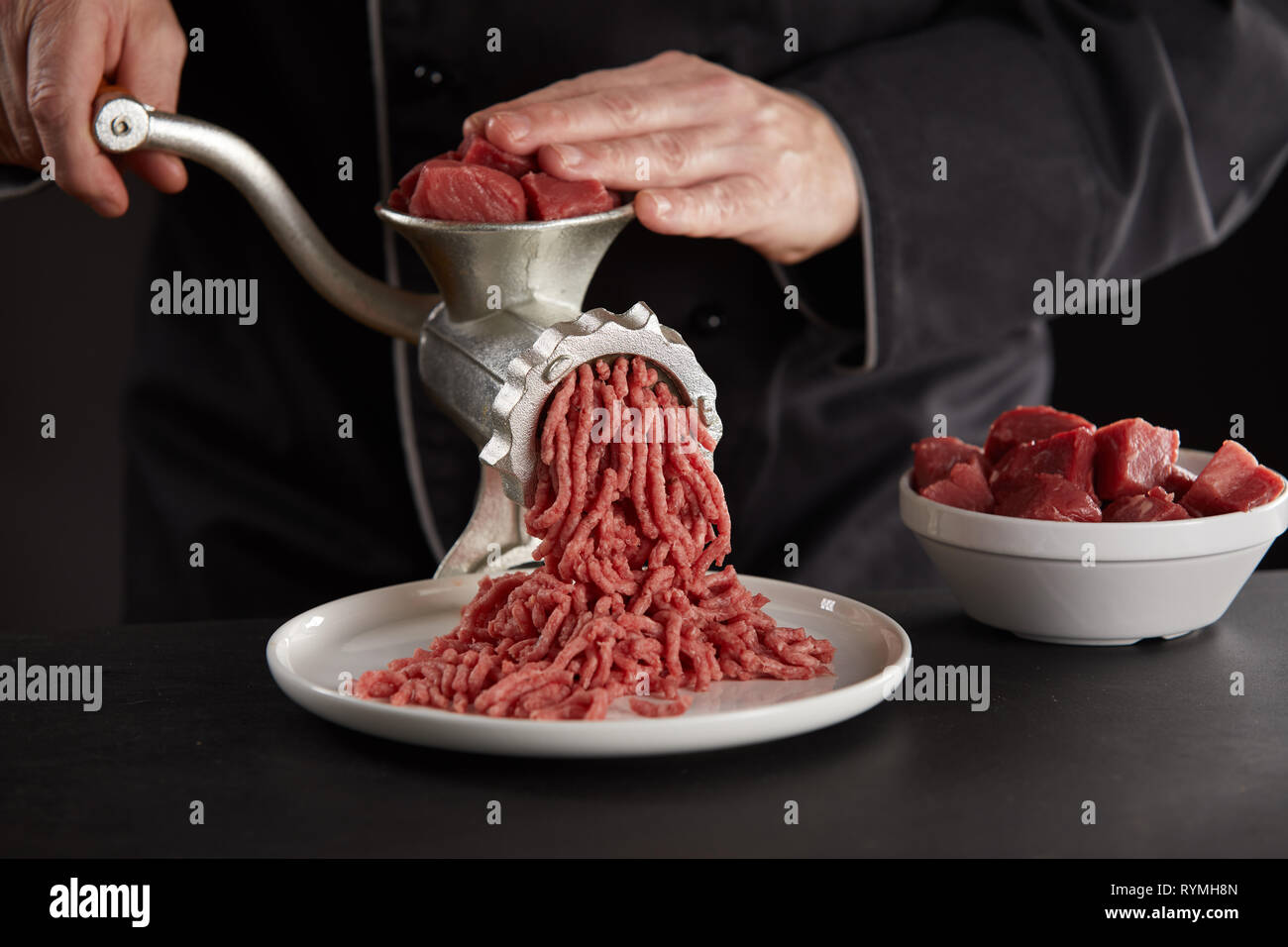 https://c8.alamy.com/comp/RYMH8N/man-in-black-uniform-making-minced-meat-of-beef-or-pork-with-old-metal-manual-grinder-pieces-of-fresh-red-meat-for-mincing-in-white-bowl-process-of-RYMH8N.jpg