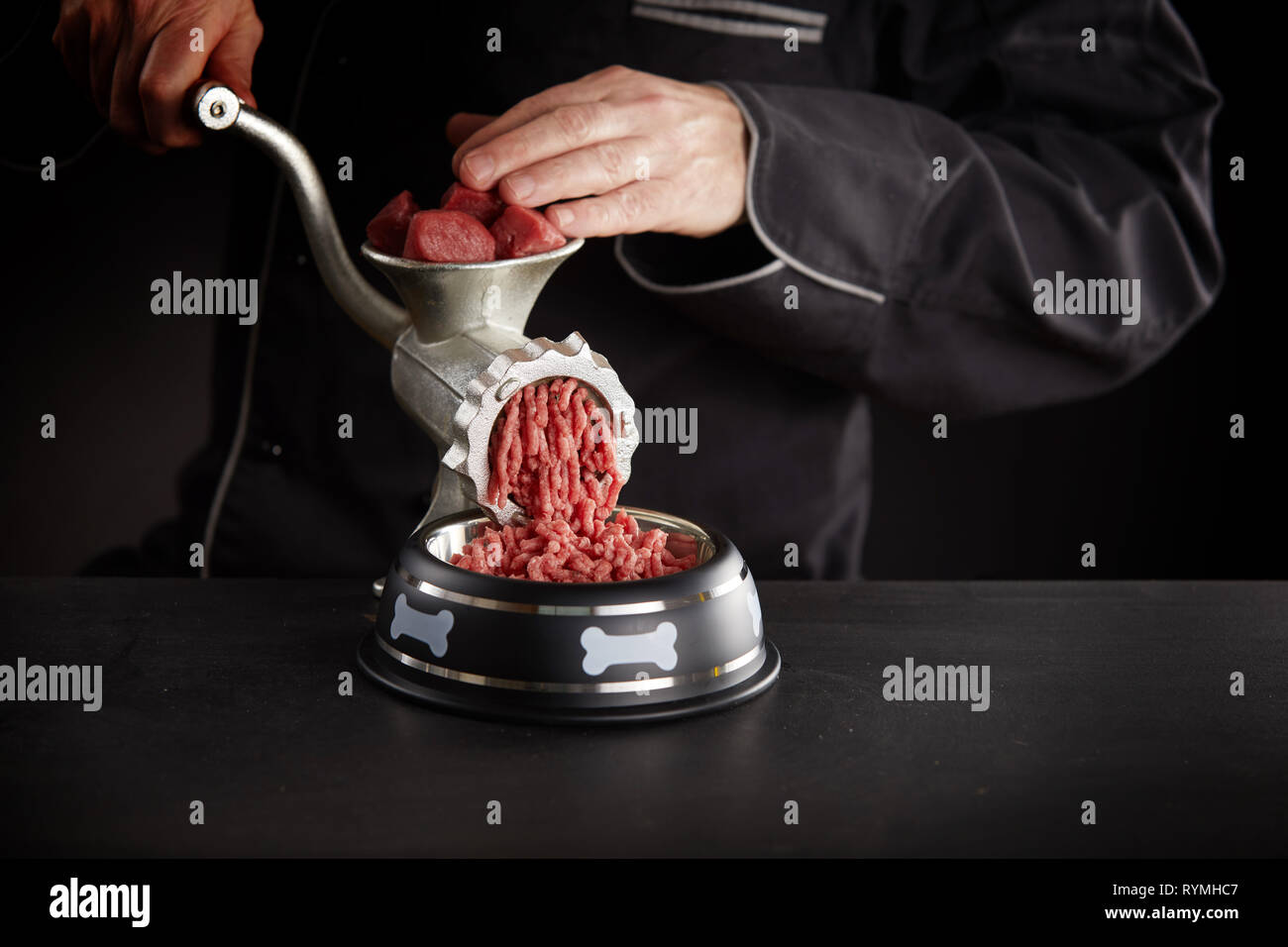 https://c8.alamy.com/comp/RYMHC7/man-making-minced-meat-for-dog-pushing-it-through-old-metal-manual-meat-grinder-into-dog-bowl-viewed-against-black-background-in-close-up-RYMHC7.jpg