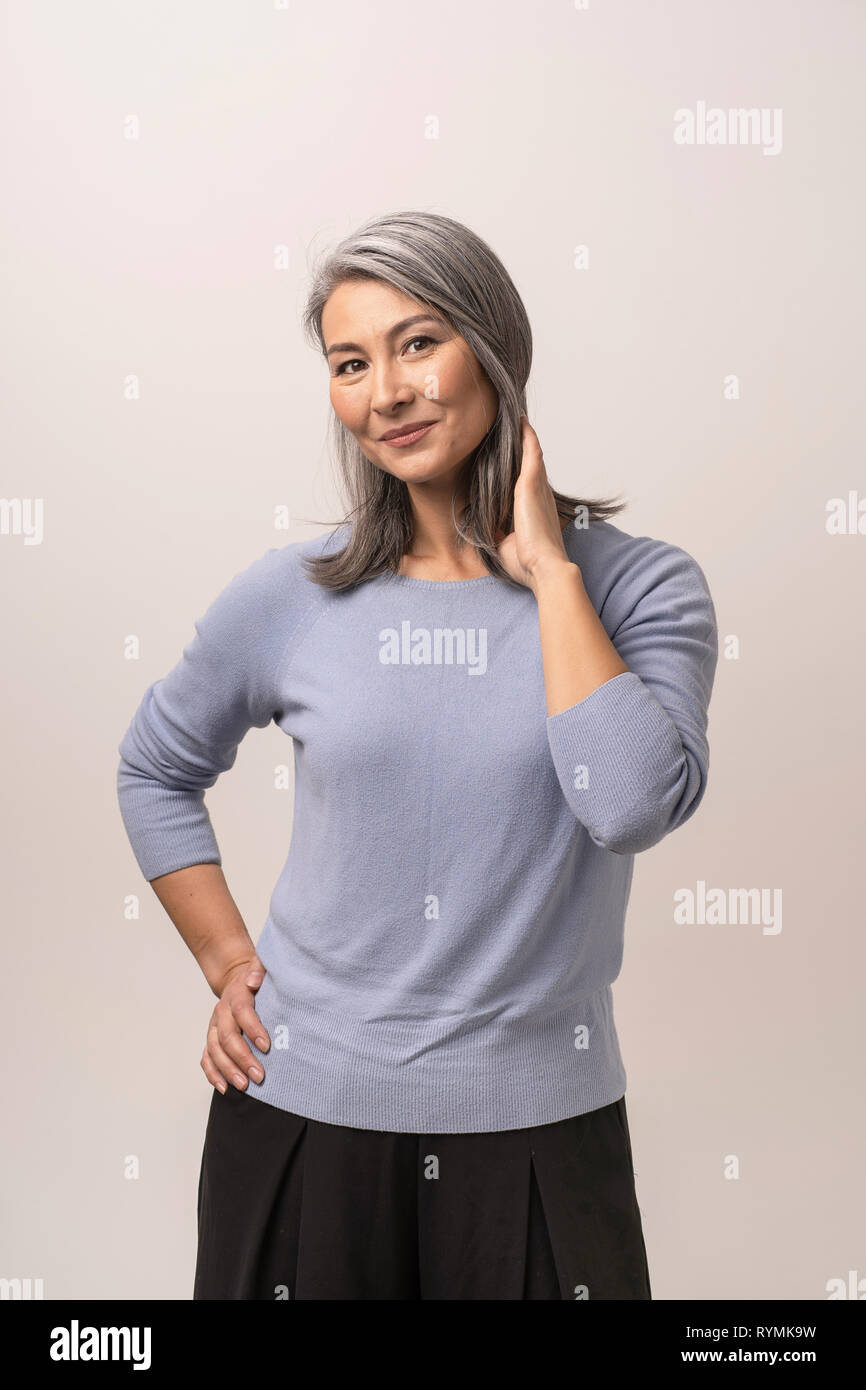 Smiling Asian woman touches her grey hair Stock Photo