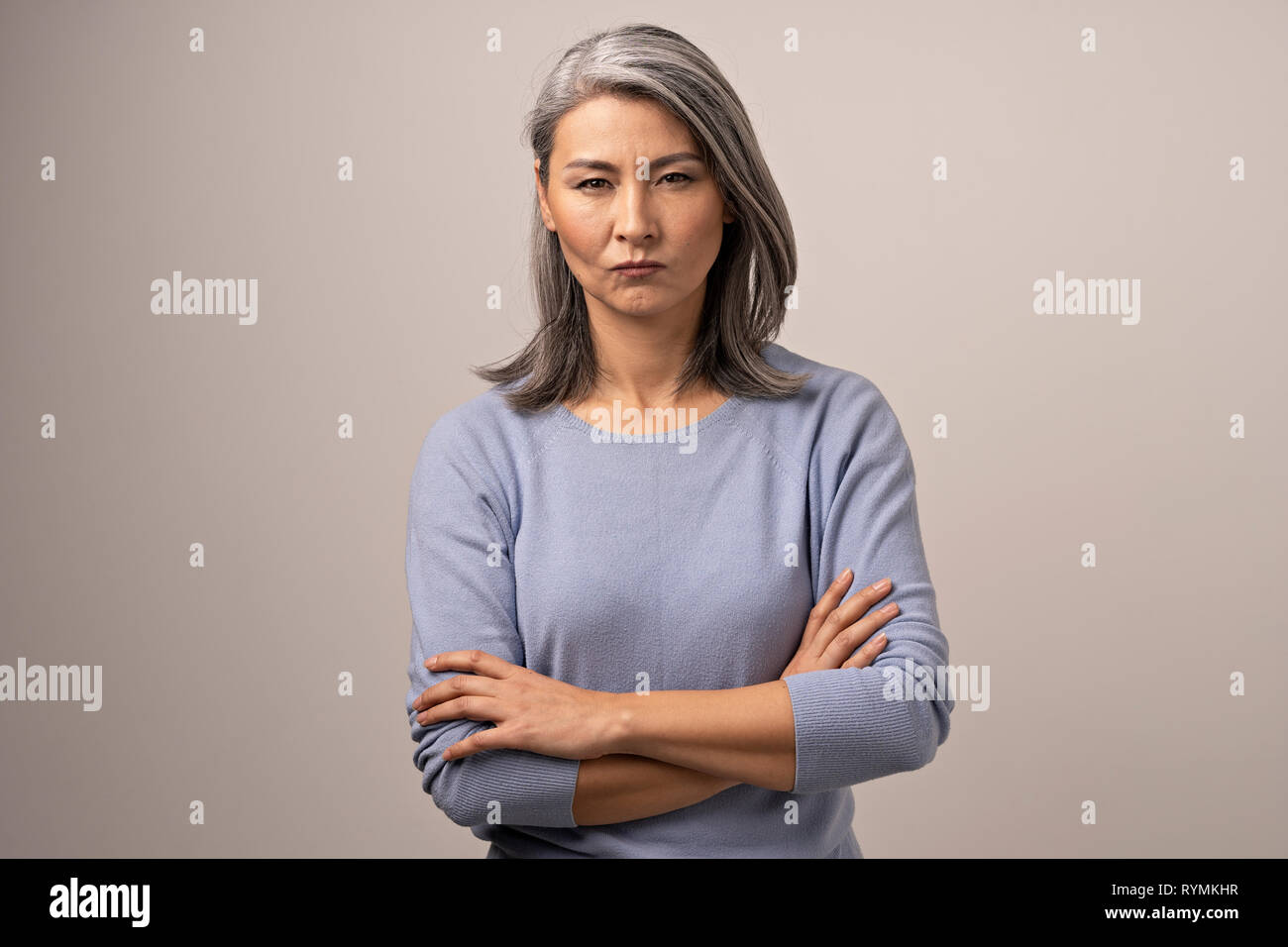 Serious Mongolian Woman with Gray Hair Against the Backdrop of Gray. Stock Photo