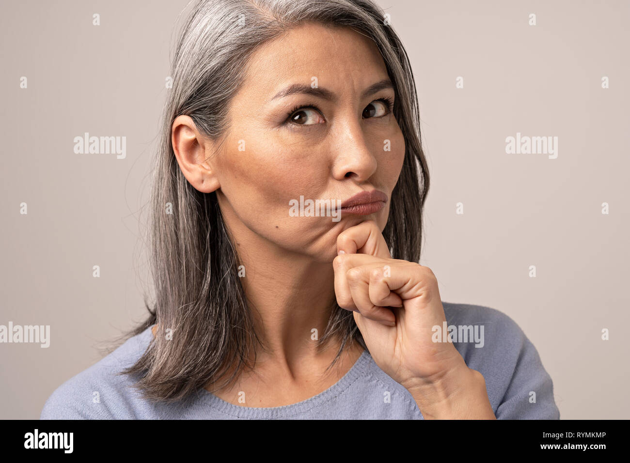 Beautiful mature woman blows lips while touching her chin Stock Photo