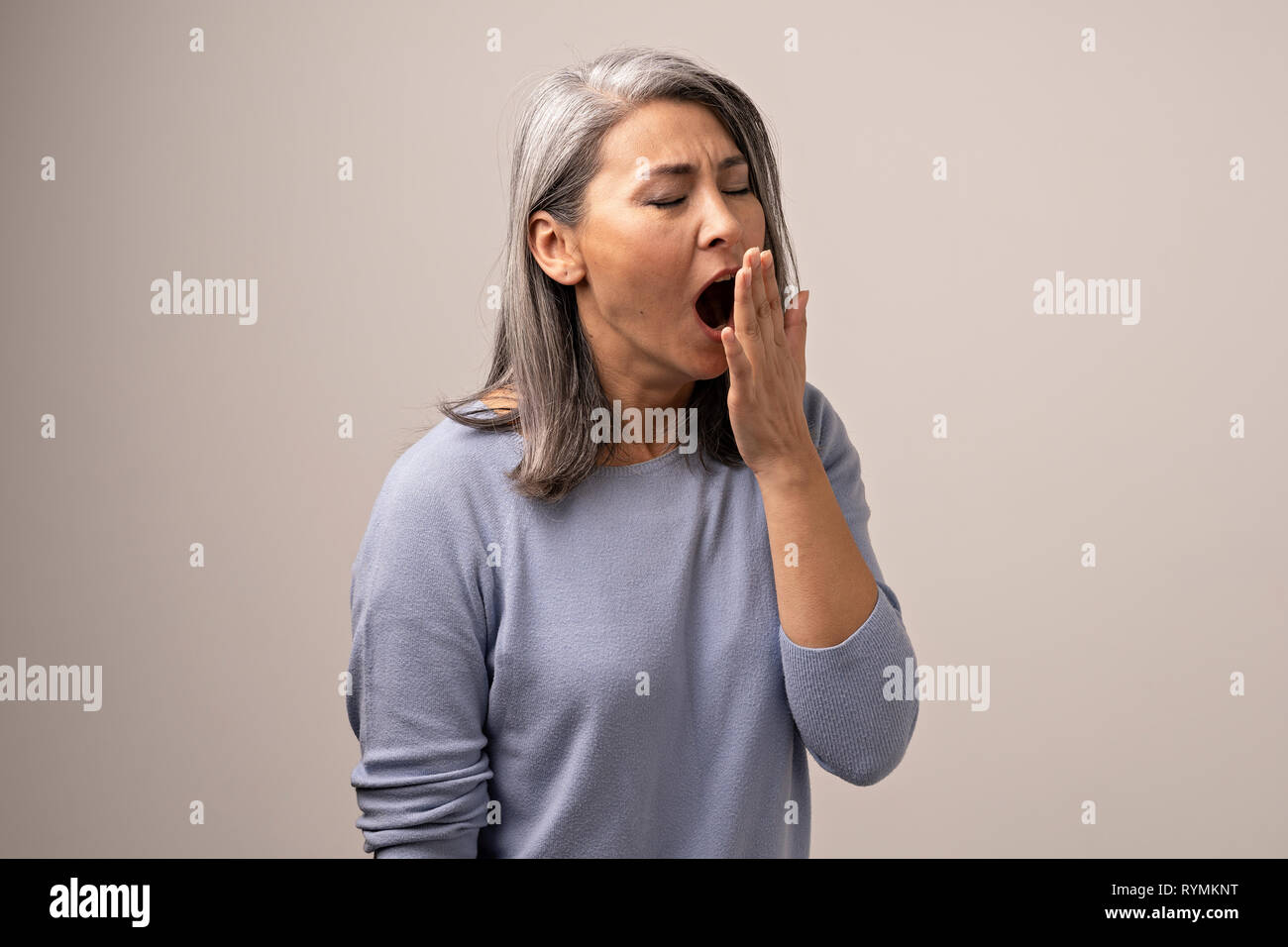 Sleepy Gray Haired Mongolian Woman on a Gray Background. Stock Photo
