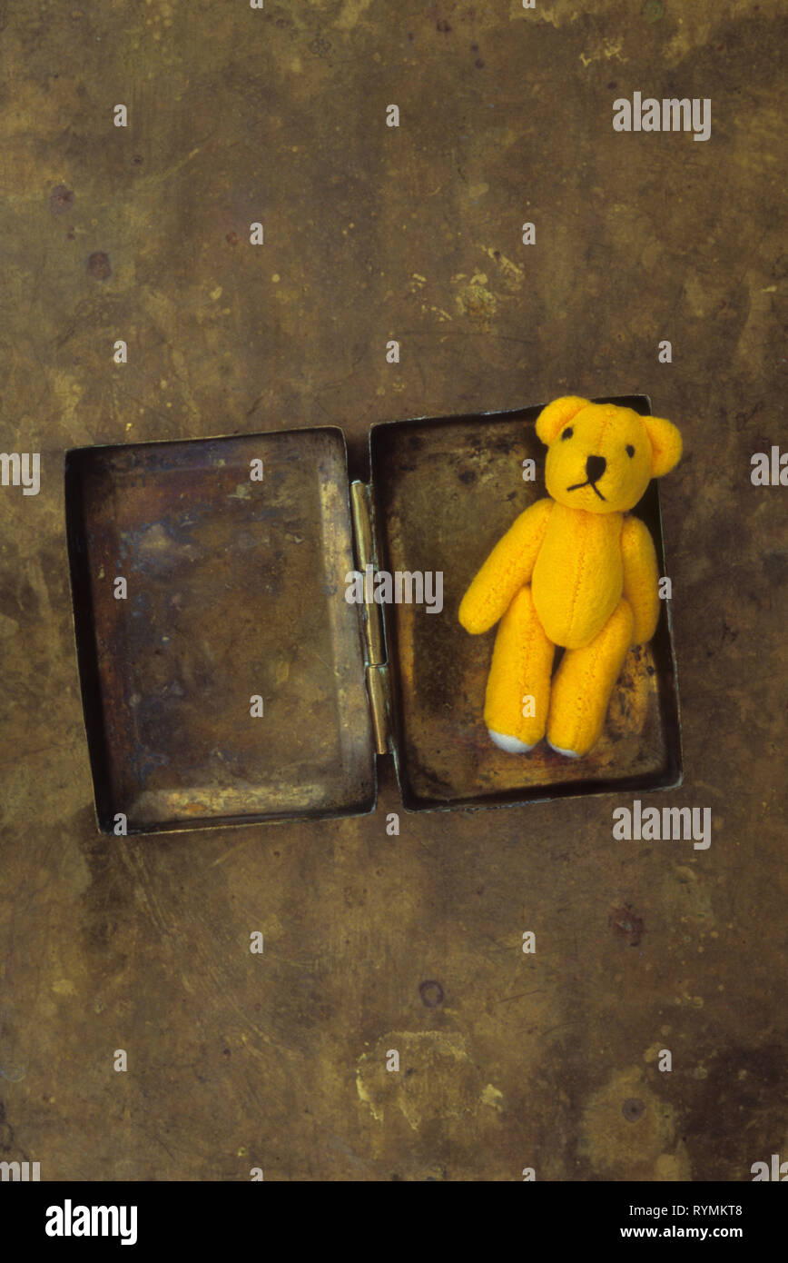 Miniature yellow teddy bear lying in small tarnished brass box Stock Photo