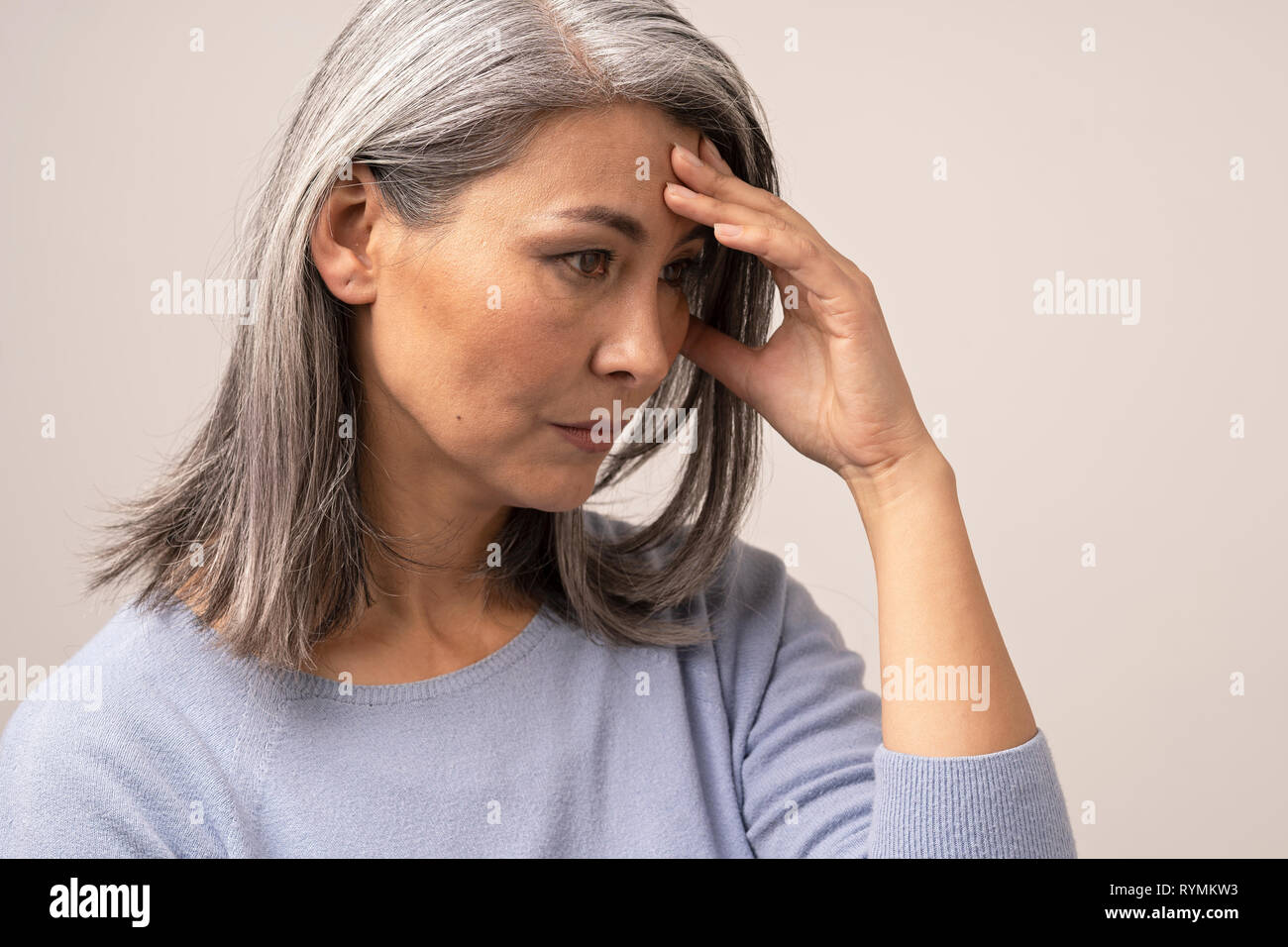 Mature Asian woman touches her forehead in distress Stock Photo