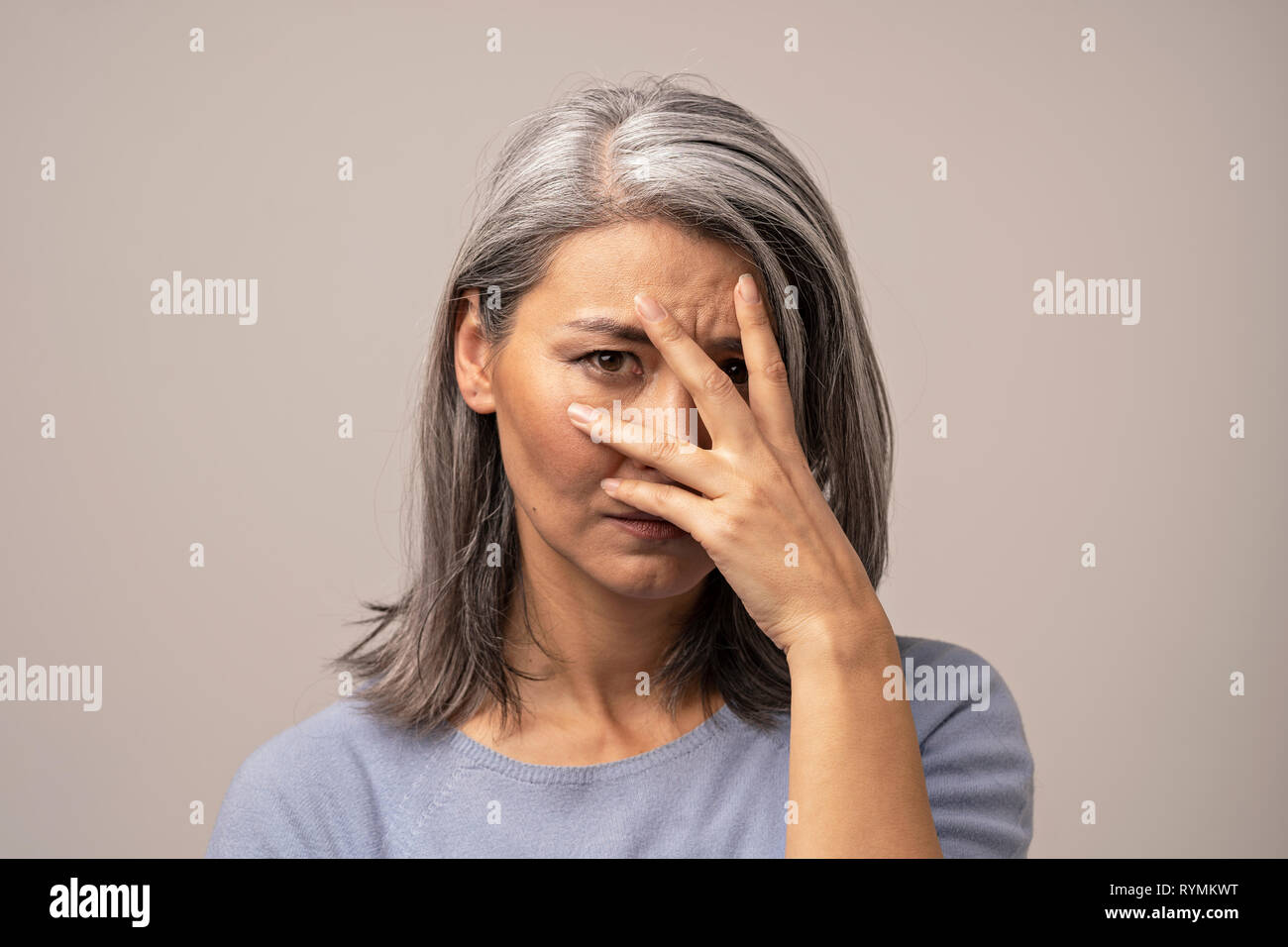 Woman of Mongolian Appearance with a Sad Look on a Gray Background. Stock Photo