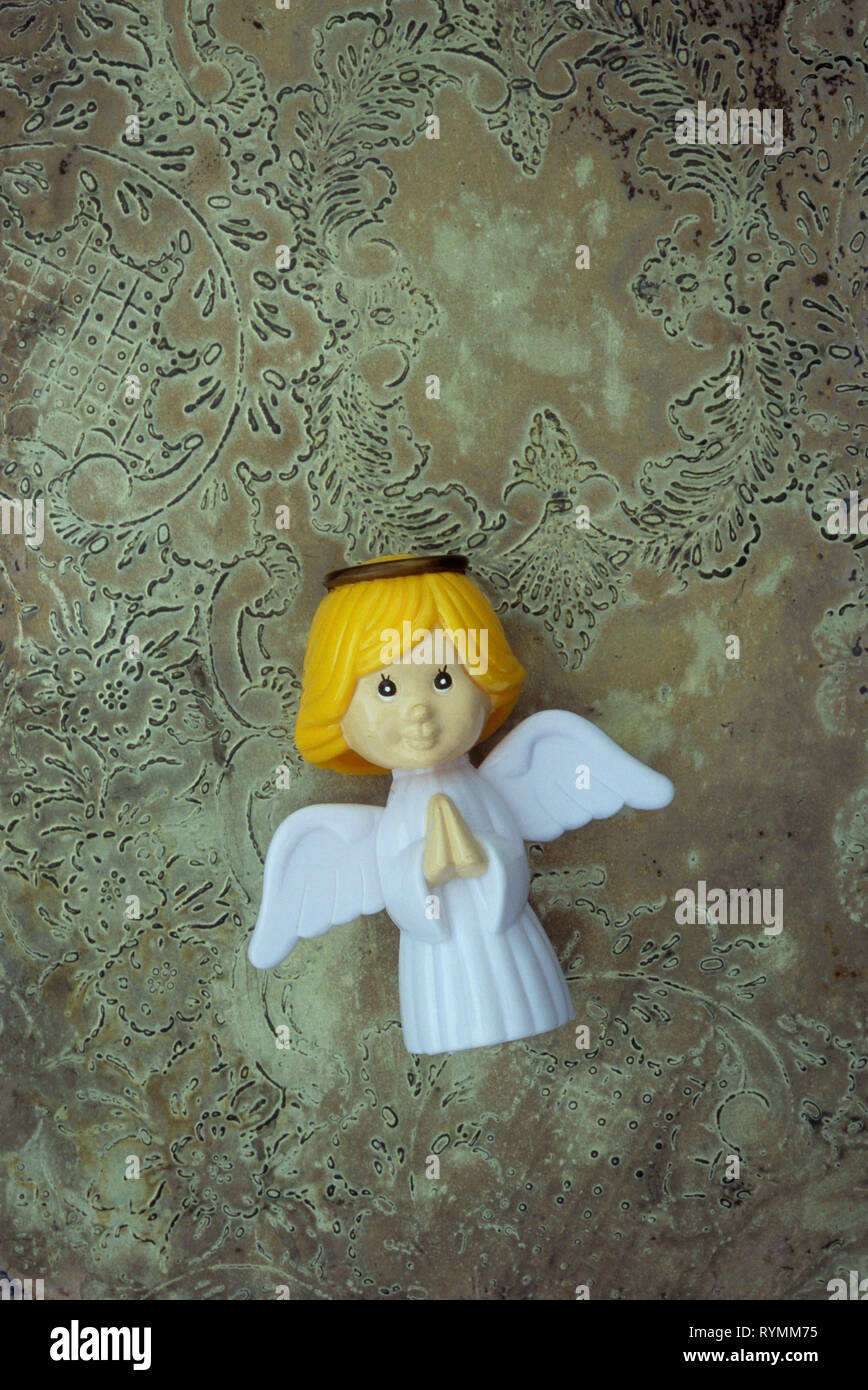 Plastic model of modern angel with hands clasped in prayer lyingon tarnished patterned silver Stock Photo