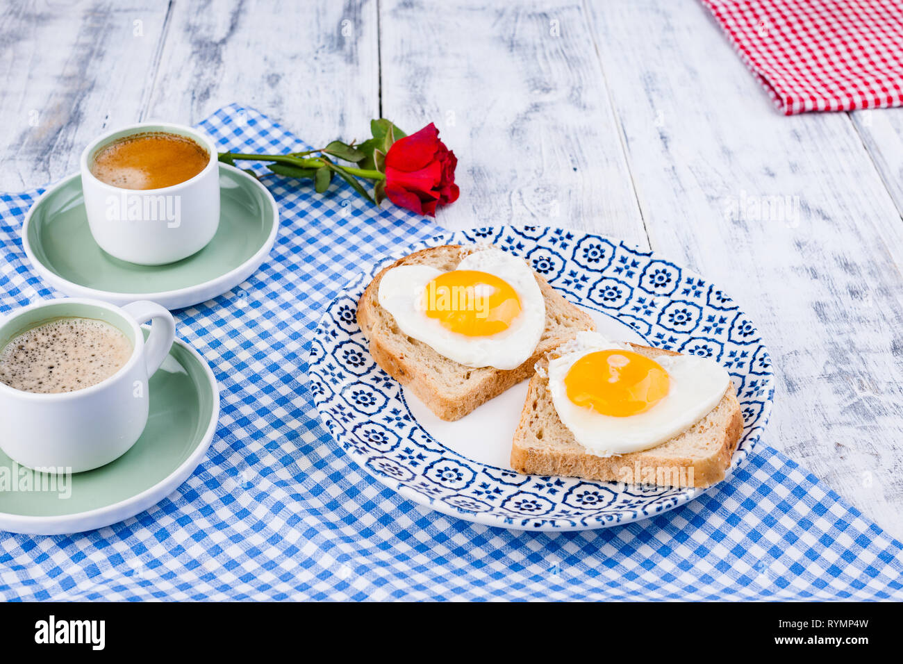 Two cups of aromatic coffee and heart-shaped toasts for a romantic morning of lovers. Red rose and morning surprise for breakfast. The concept of Vale Stock Photo