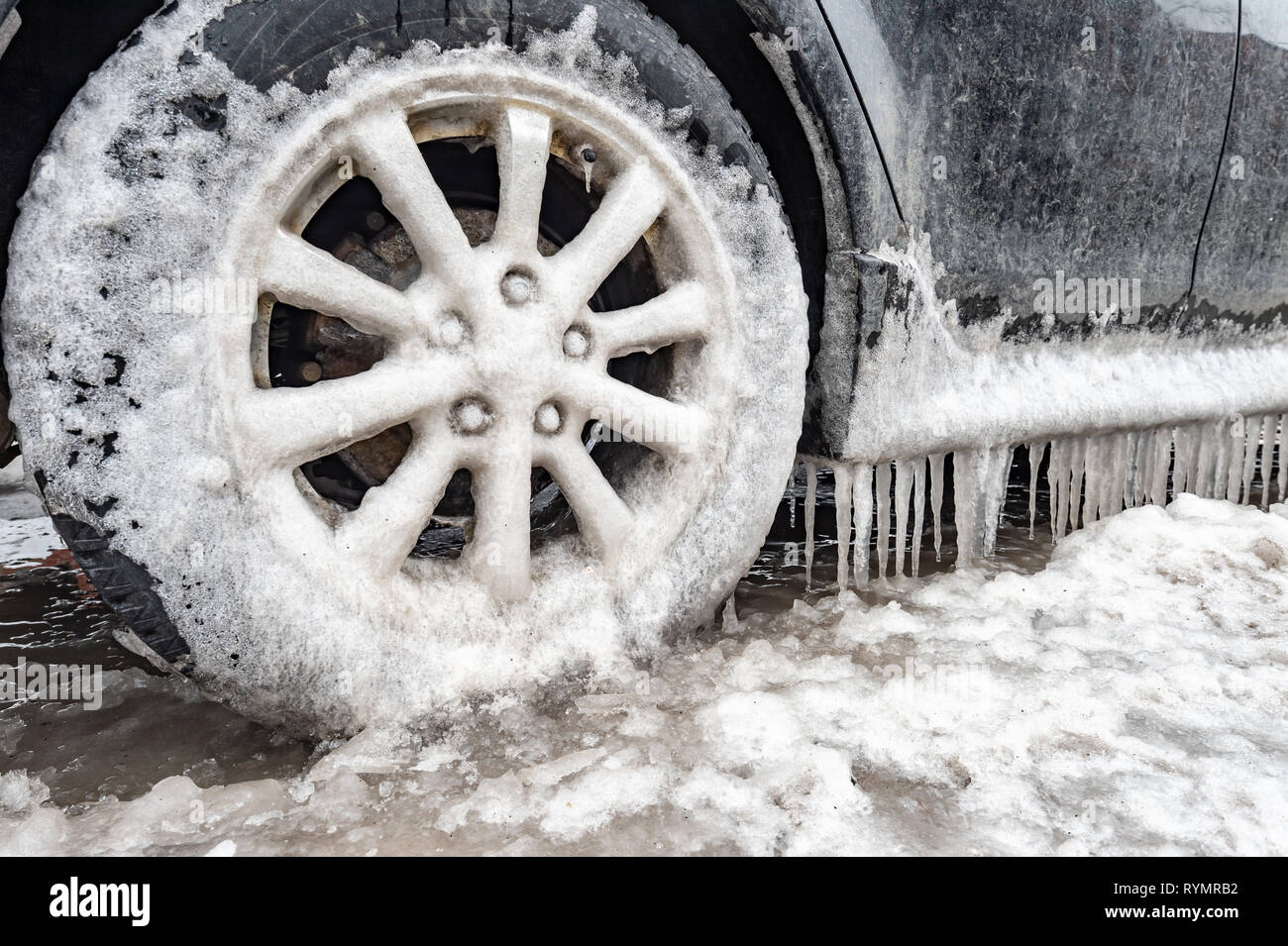 Ice buildup and icicles on a car and closeup of a frozen wheel, in